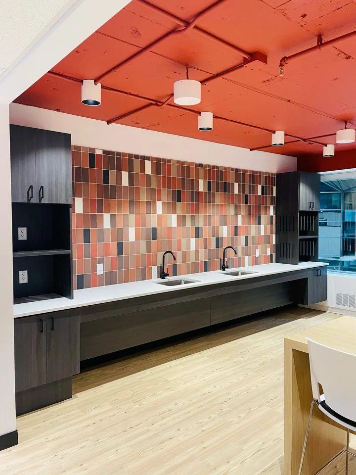 Modern kitchenette with two sinks, black faucets, colorful tiled backsplash, dark cabinets, and a large window.