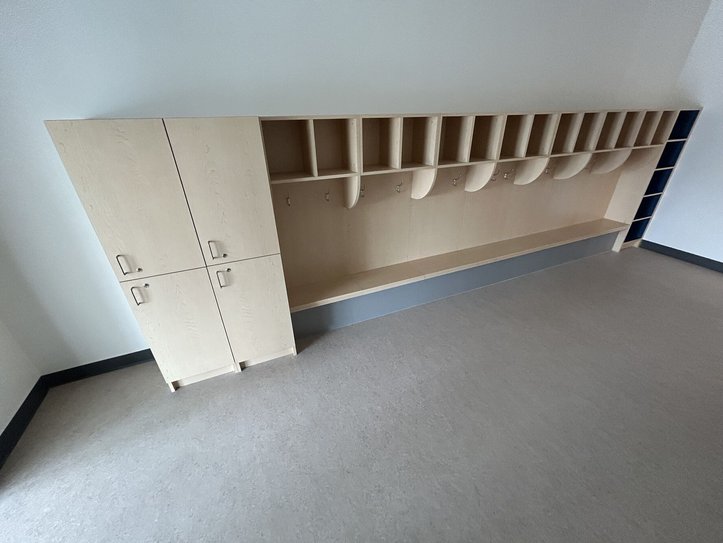 A wooden storage unit with cubbies and hooks, positioned against a wall in a room with gray carpet.