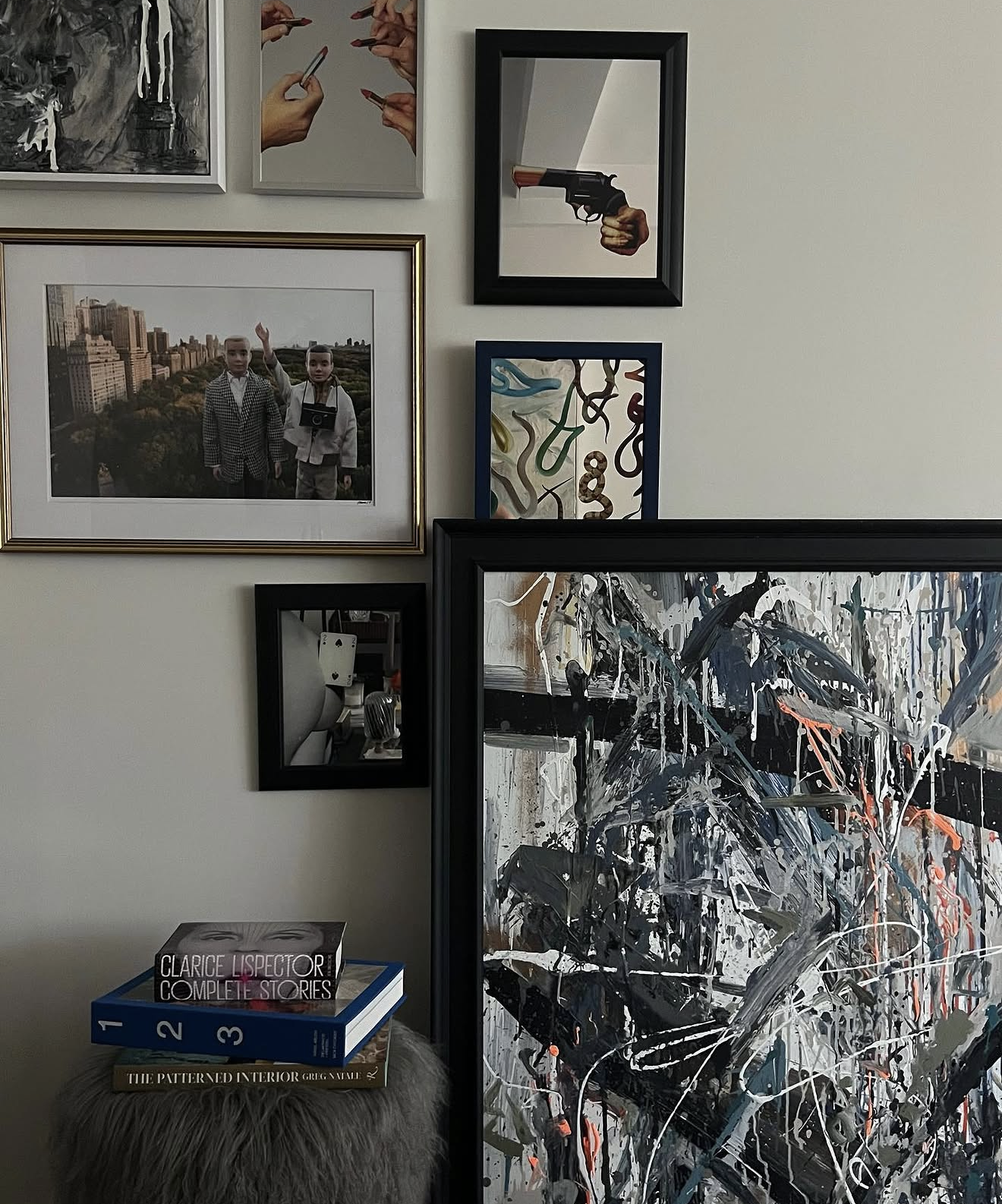 A wall decor with a gallery of framed pictures, paintings, and artwork. There is a framed photograph of two children, one with a camera, in a city park. Other frames contain an artwork of hands holding pens, a hand holding a gun, a colorful abstract 