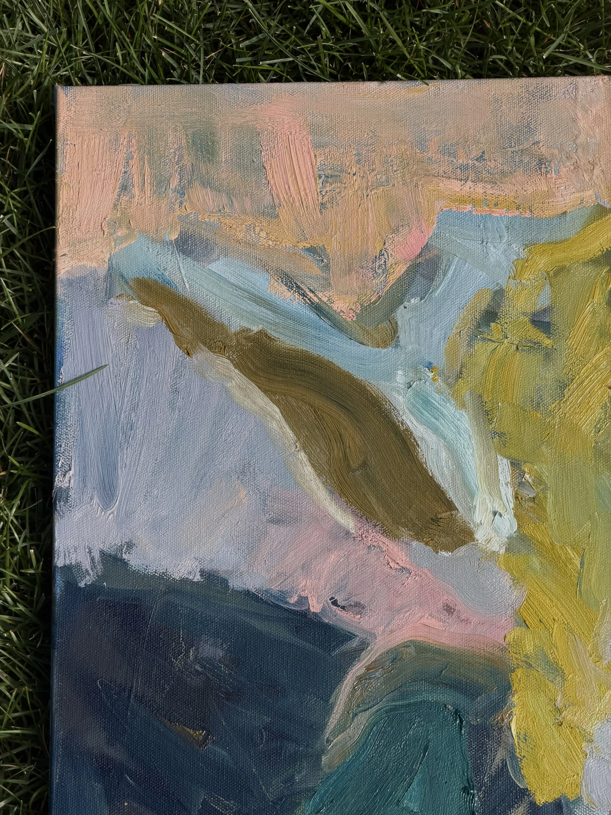 Close-up of a colorful abstract oil painting with brushstrokes of pink, blue, yellow, and brown, resting on grass.