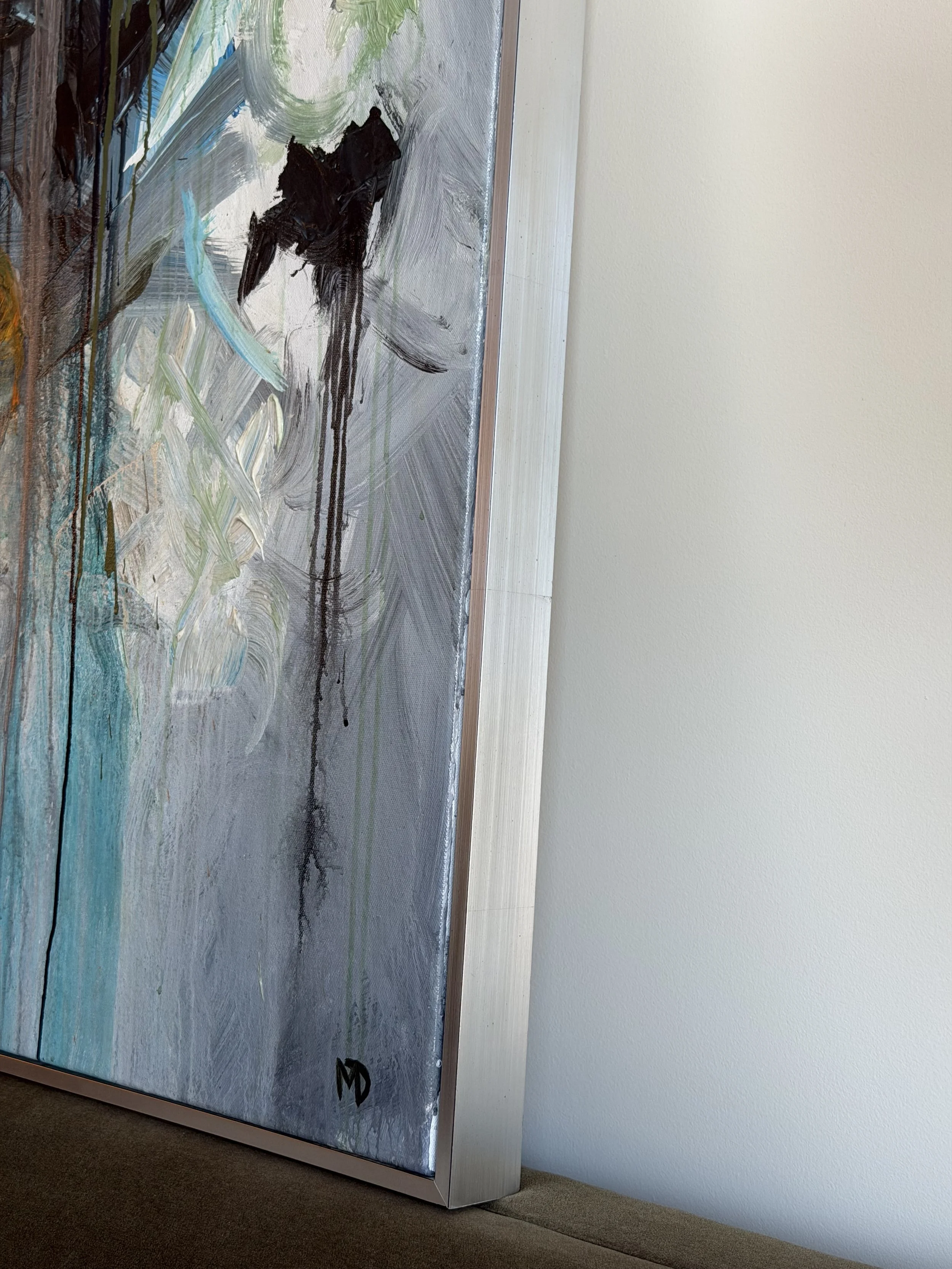 Abstract painting with brushstrokes in black, white, green, and blue colors on a vertical canvas, leaning against a wall in a room.