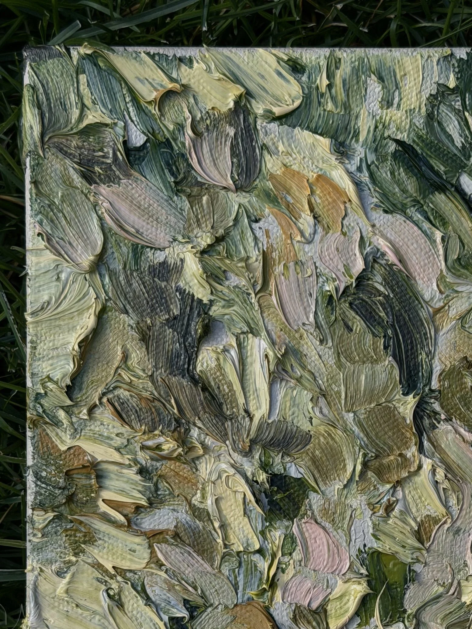 A piece of abstract art with swirling brush strokes in shades of green, yellow, black, and pink, laid on grass.