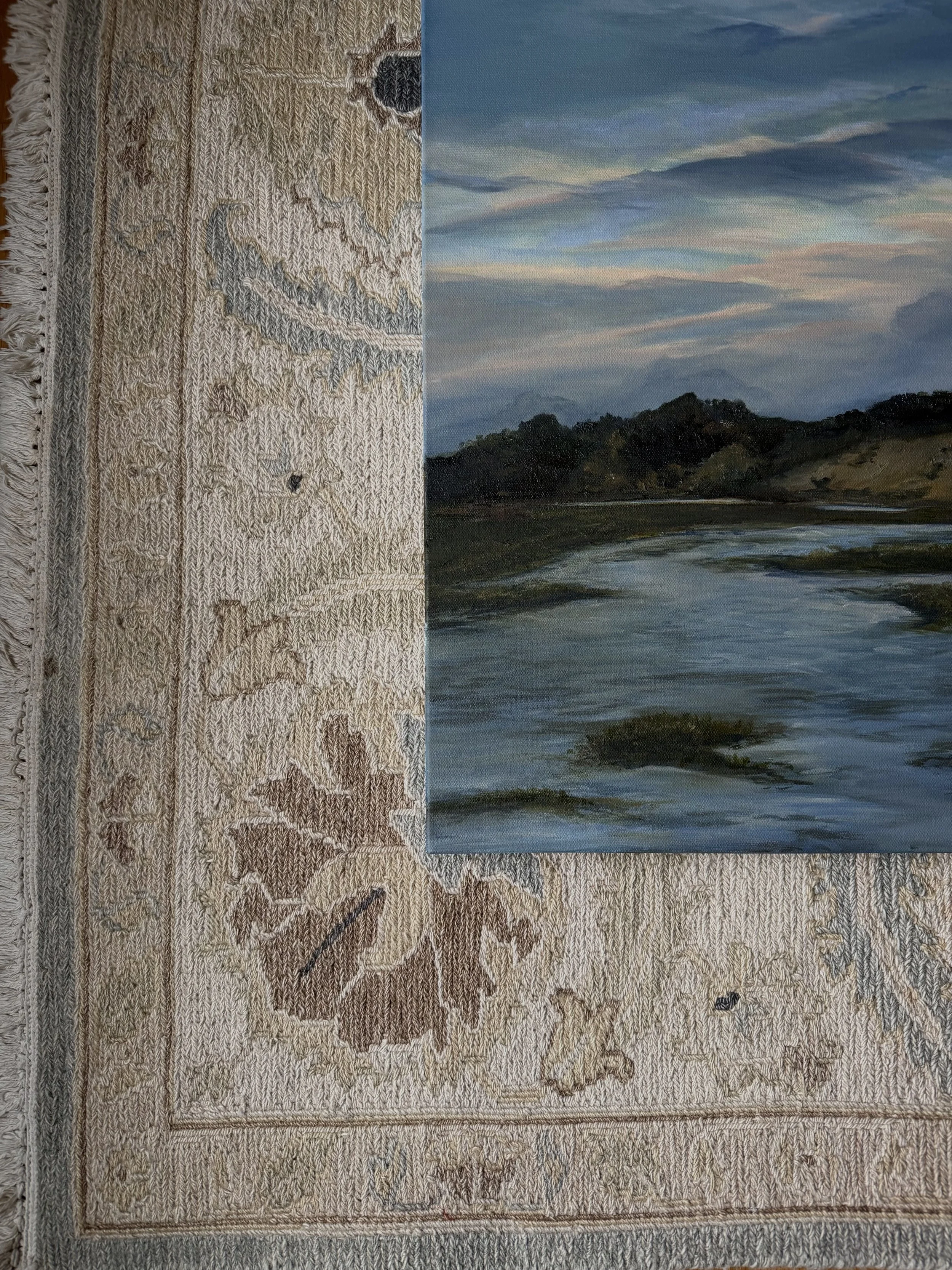 A landscape painting of a river with green trees and mountains in the background under a sky with wispy clouds.