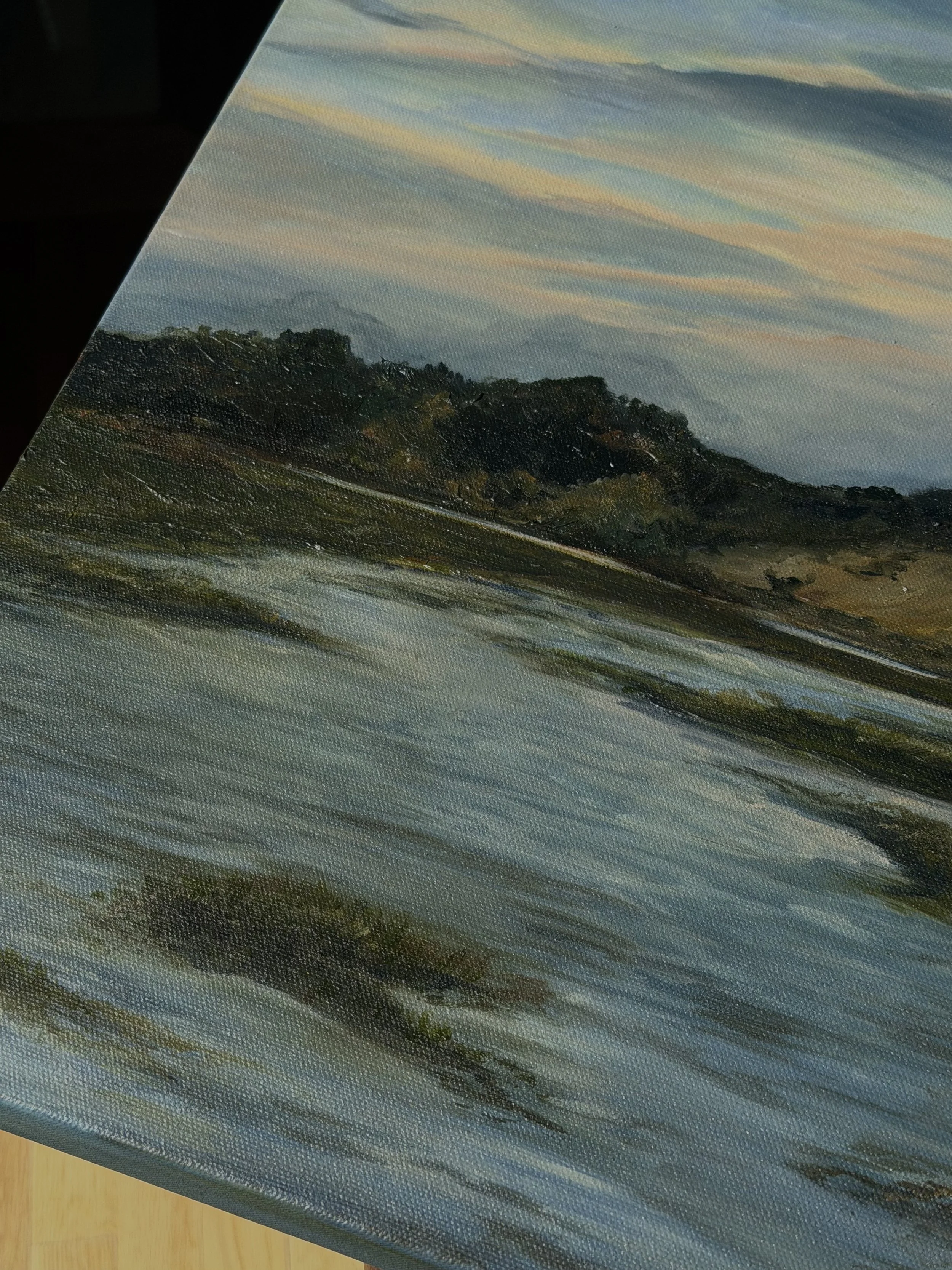 Close-up of a landscape painting depicting a sunset or sunrise over hills with trees, painted on textured canvas.