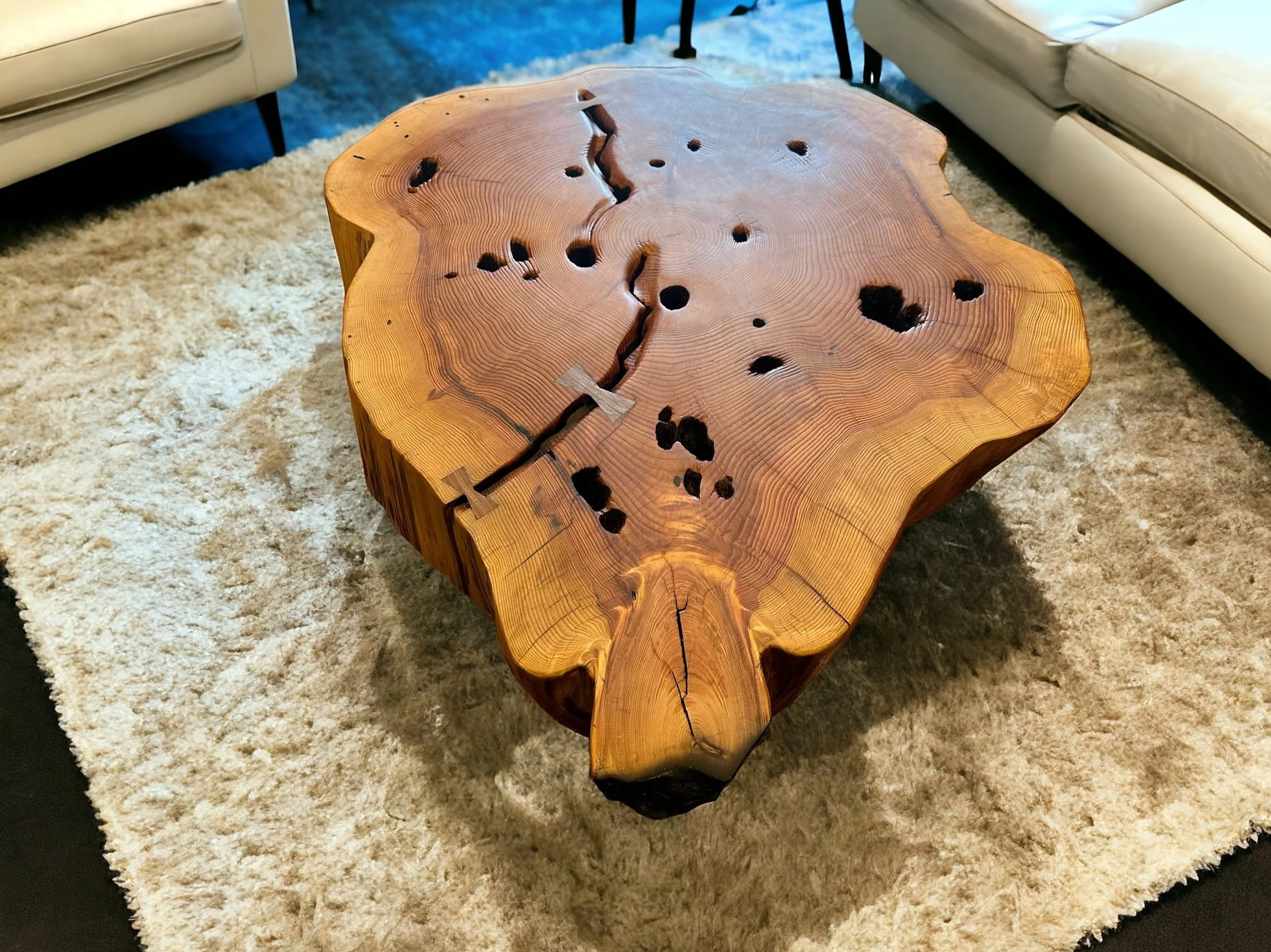 Wooden coffee table with natural edges , on a light rug between light-colored sofas in a living room.