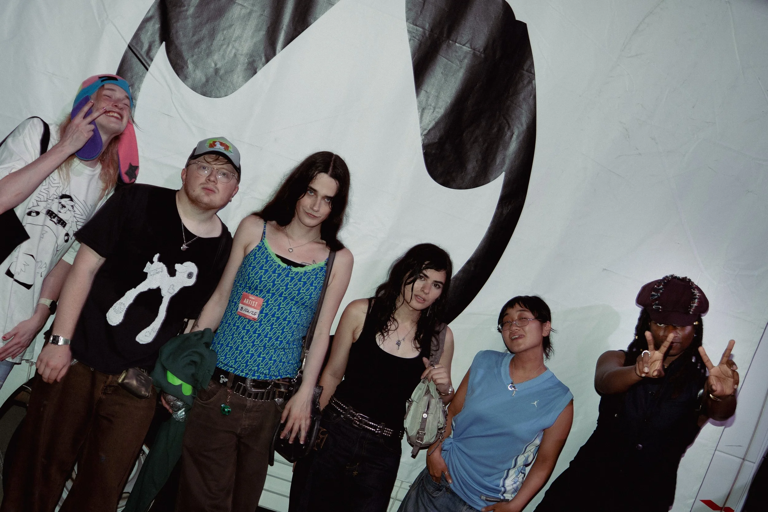 A group of diverse people smiling and making peace signs in front of a large panda illustration at an indoor event.