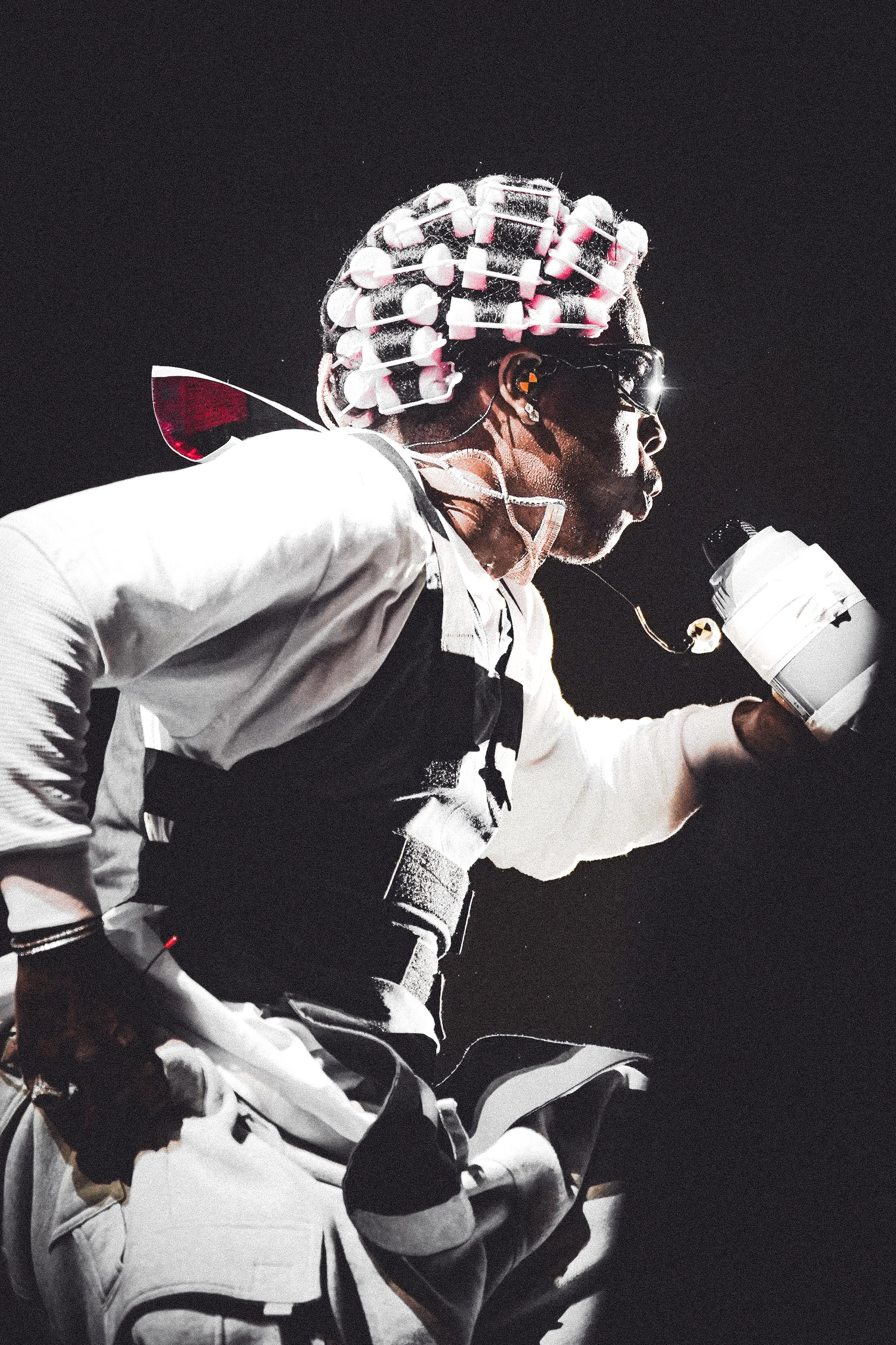 Person wearing roller skates with pink wheels, holding a white cup, wearing sunglasses, and a white and black outfit, skating outdoors at night.