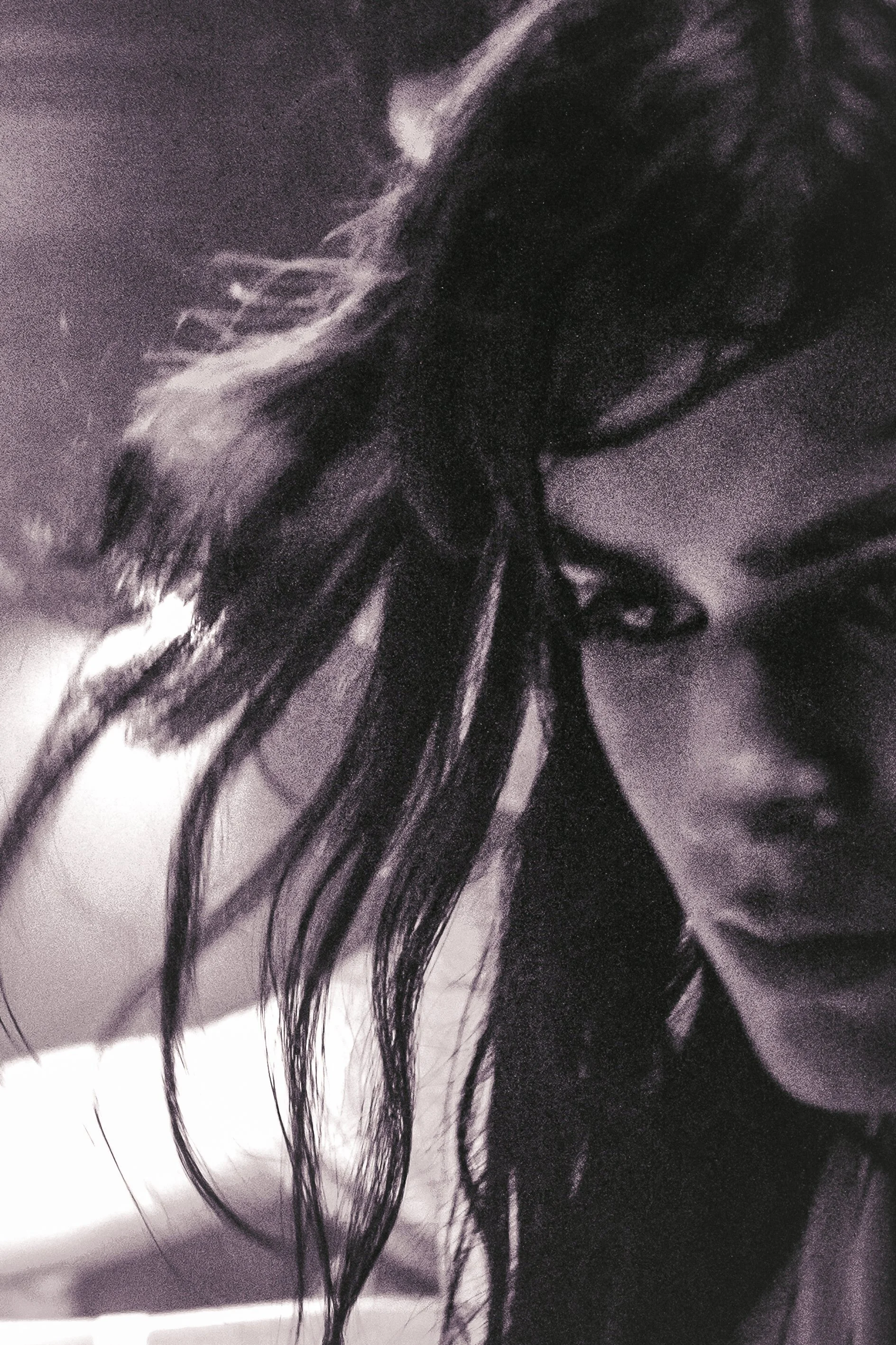 Close-up photograph of dark, slightly curly hair with some strands falling over a person's face, mostly obscuring their features.