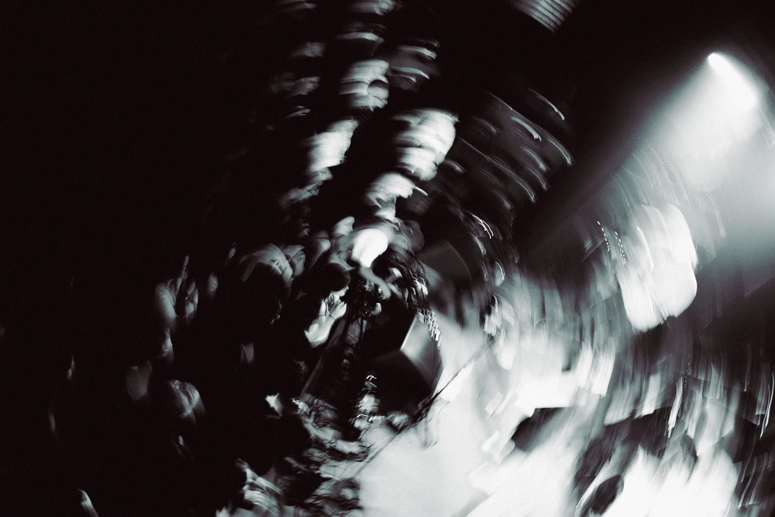 A blurred black and white photograph of a room with rows of chairs, possibly in an auditorium or conference hall, with some light at the far end.