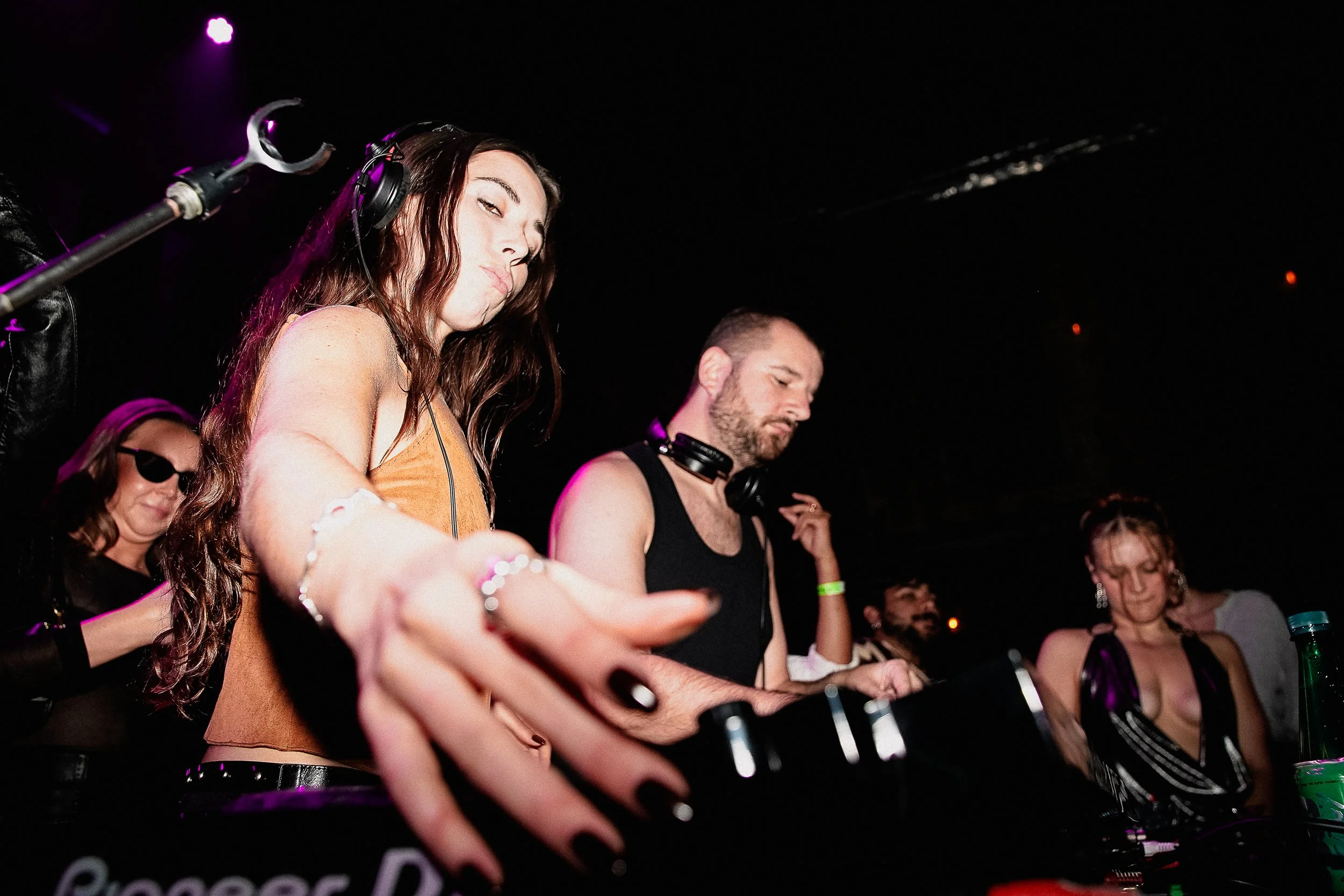 Diverse group of people DJing at an indoor event with a dark background and purple lighting.