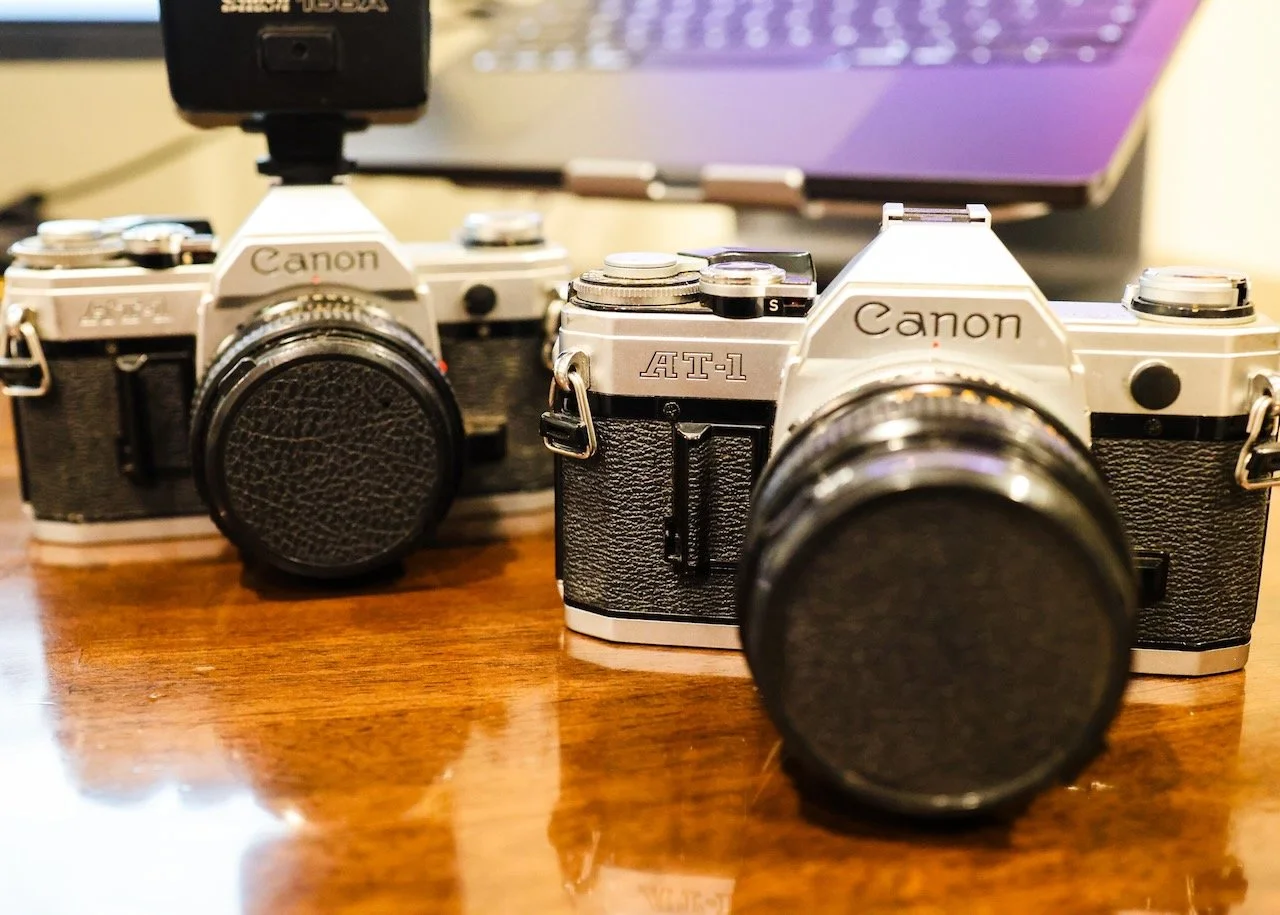 Picture of two original Canon AT-1 cameras on a desktop.