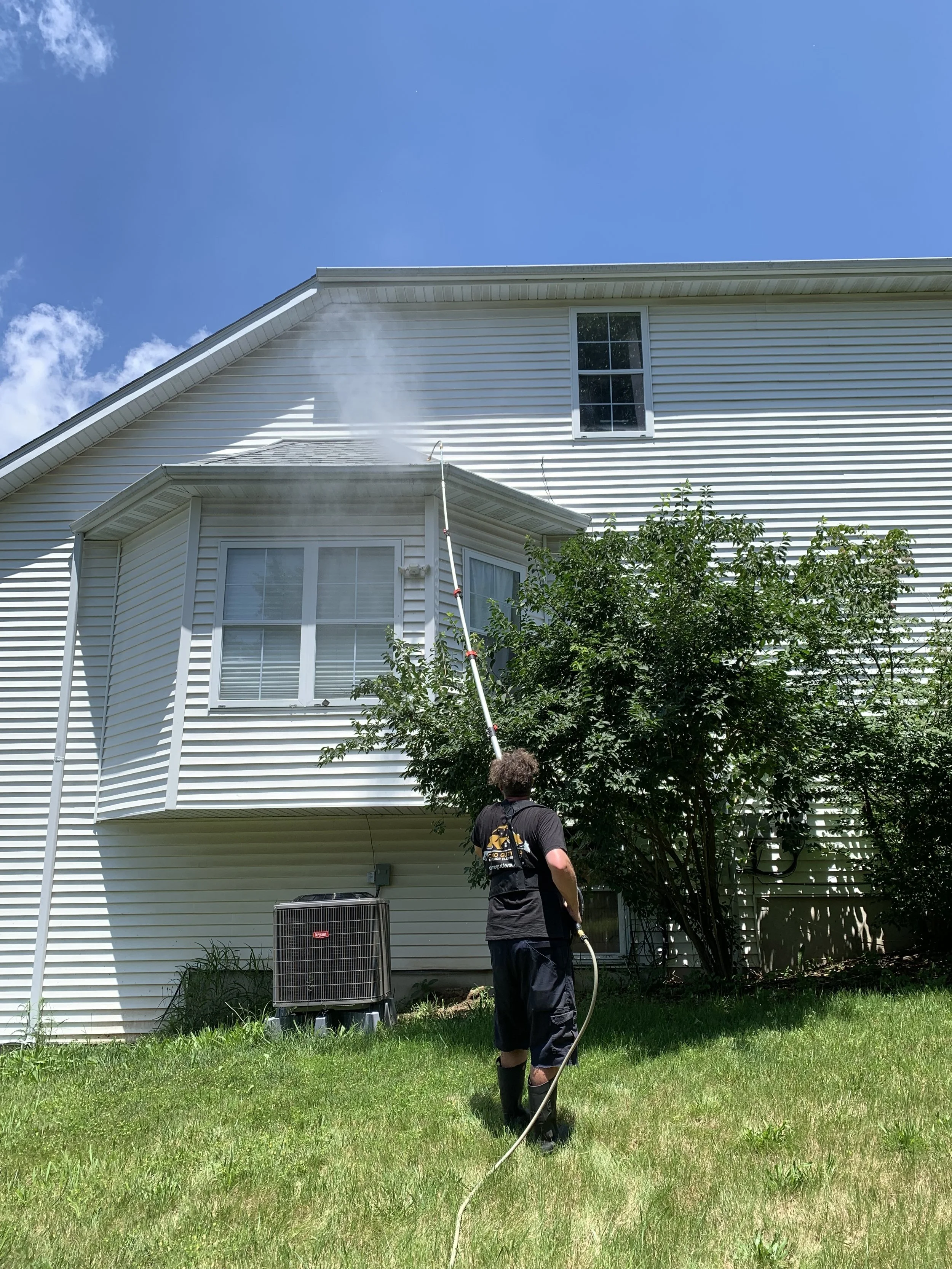 A person using a pressure washer to clean the exterior siding of a house, which has dirt and mold.