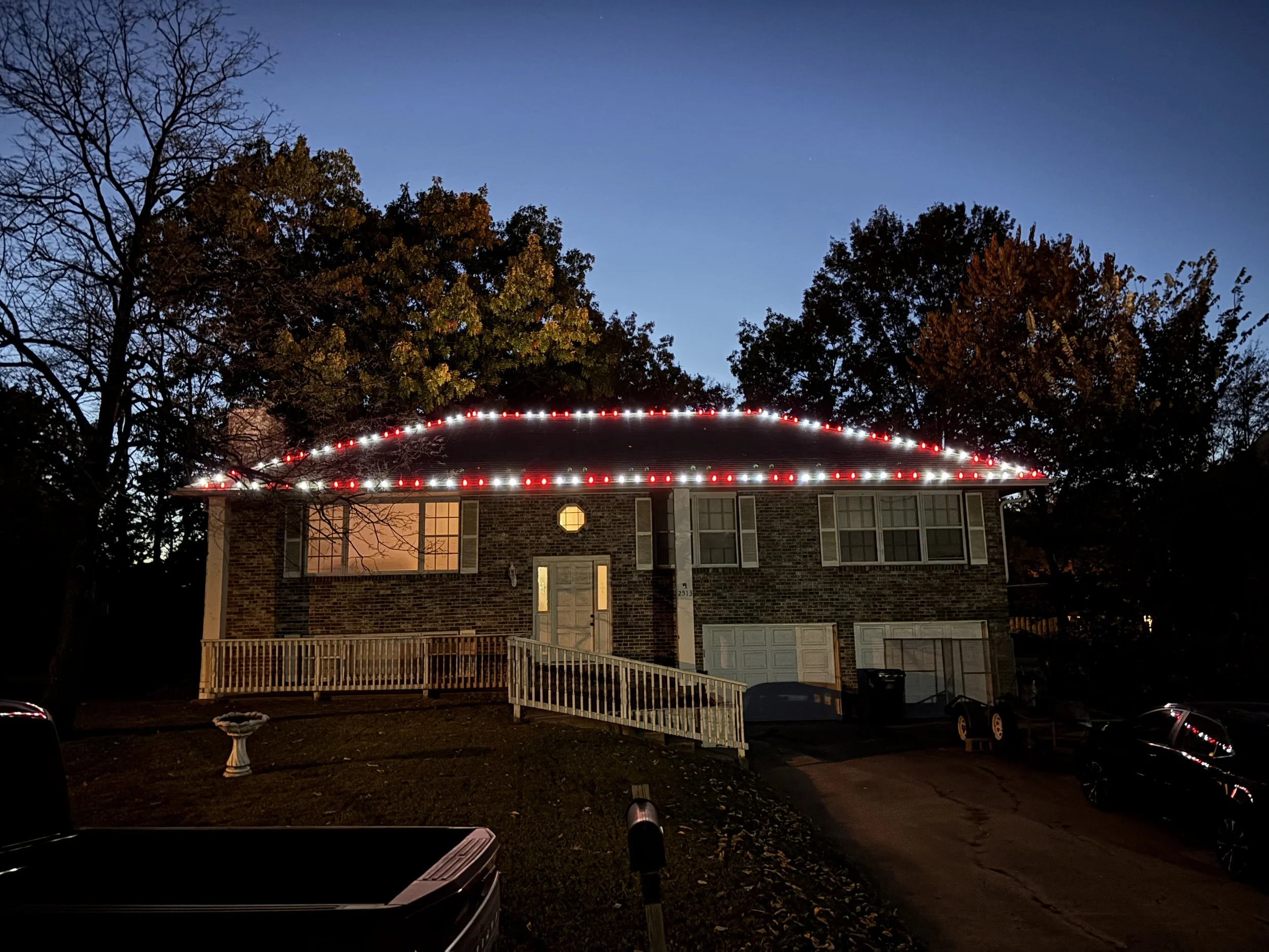 A house decorated with colorful Christmas lights on the roof and around the door, taken at night with trees in the background.