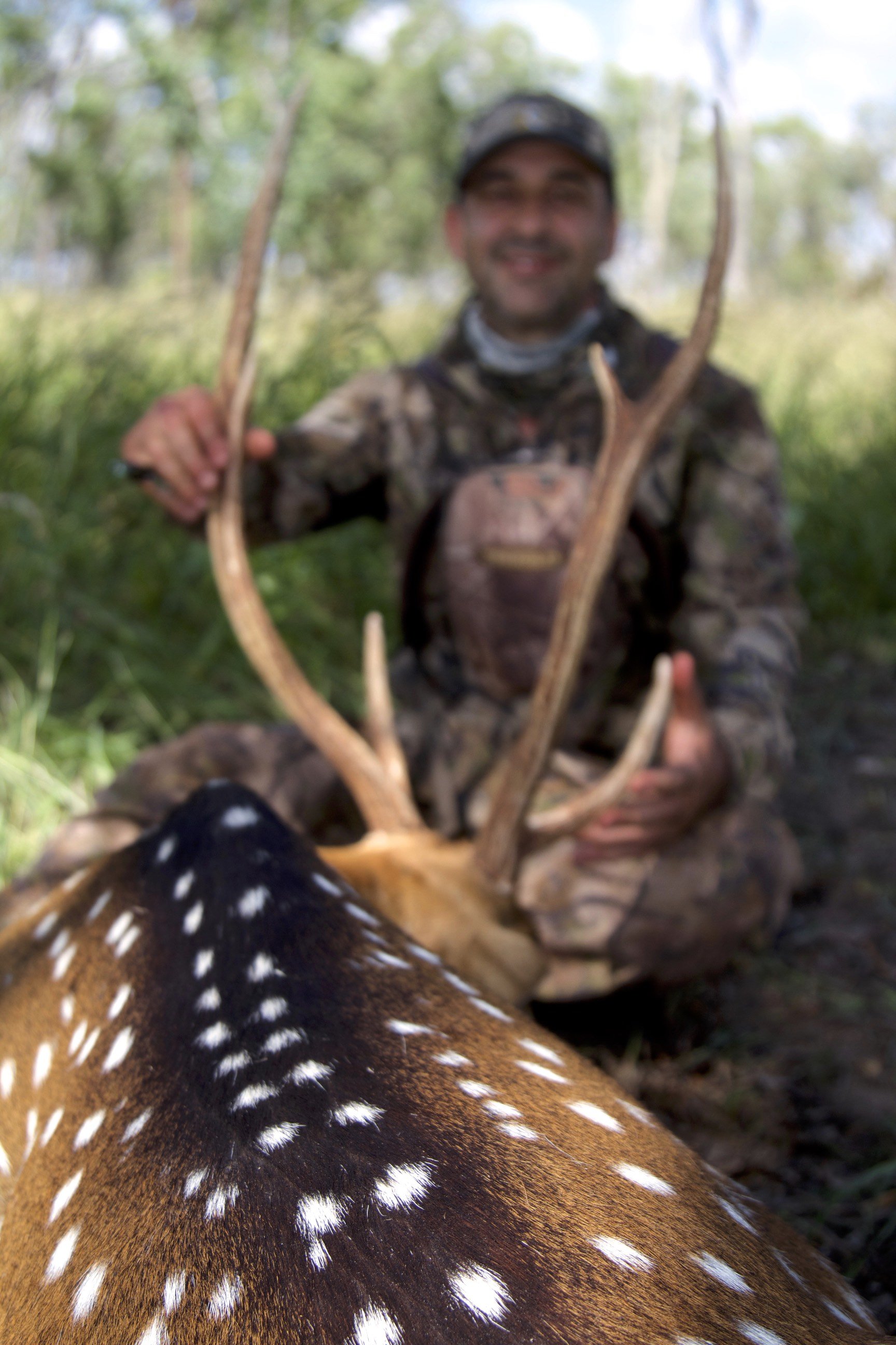 Outline of a person's face and antlers of a deer, with the person's blurred face in the background and the deer lying on the ground in the foreground.