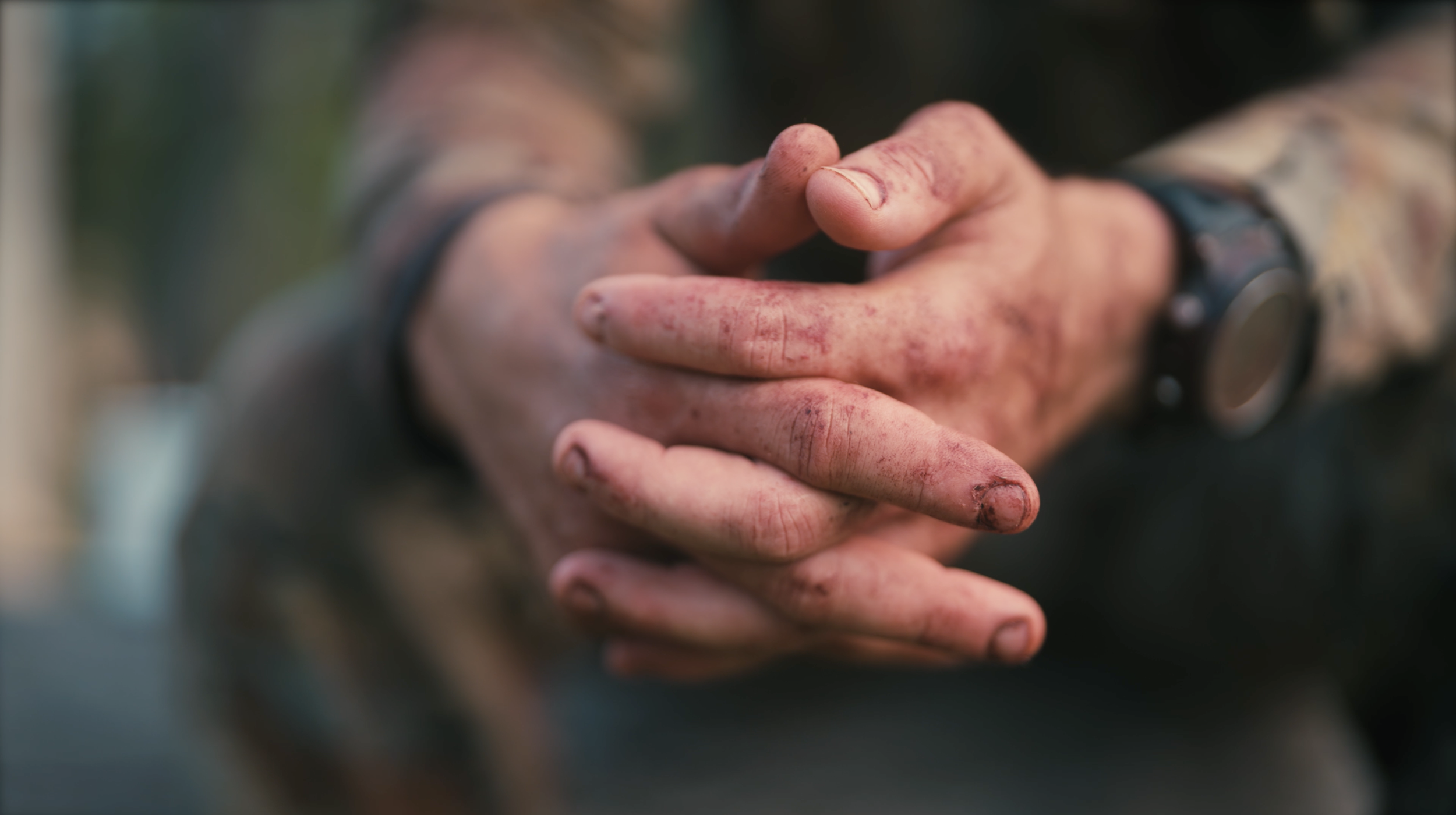 Close-up of dirty hands with mud, tangled fingers, and a watch on the wrist, suggesting outdoor work or activity.