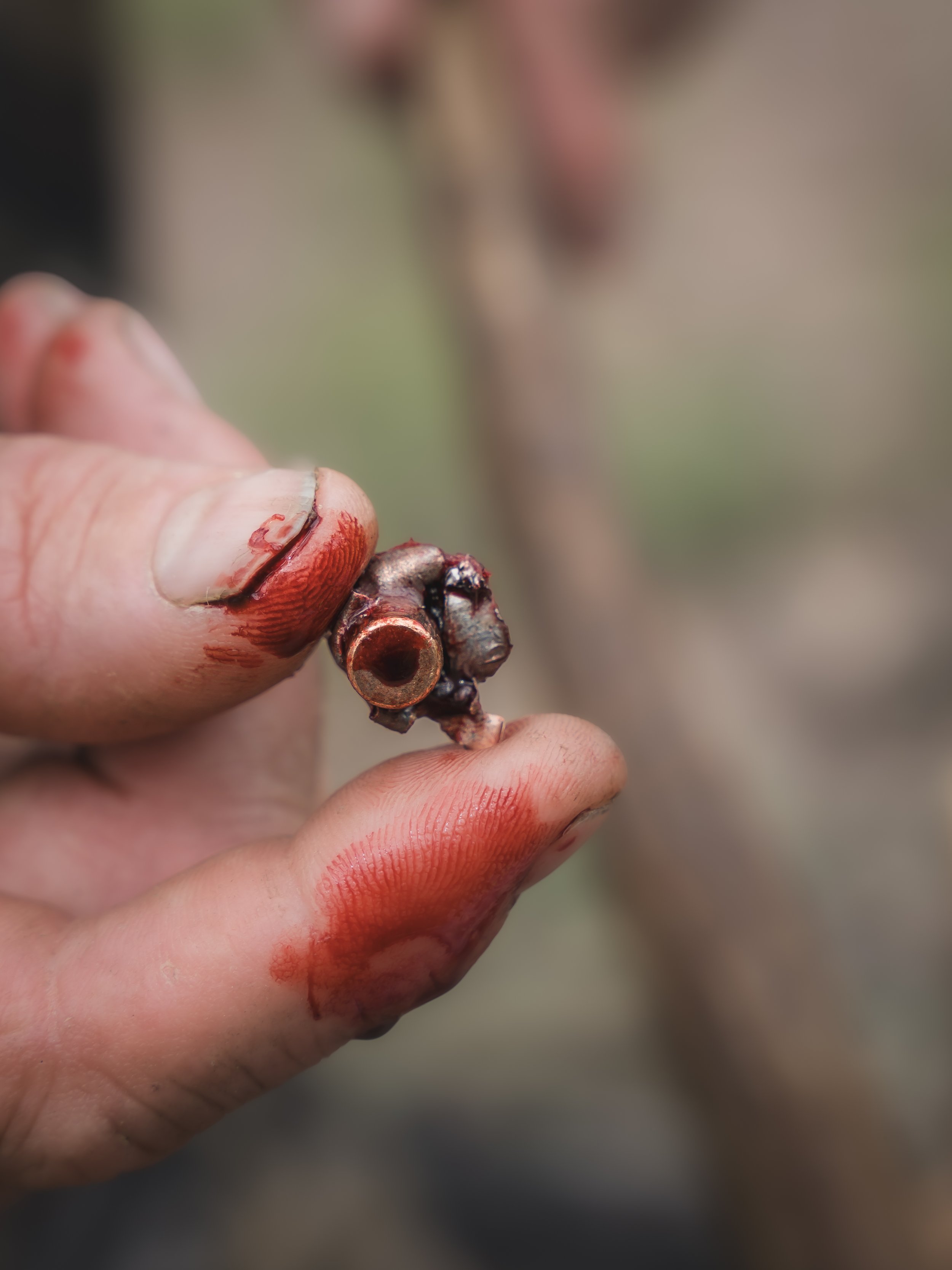 Close-up of a person's fingers holding a small, metallic object that appears to be a spark plug, with some grease and grime on the fingers.