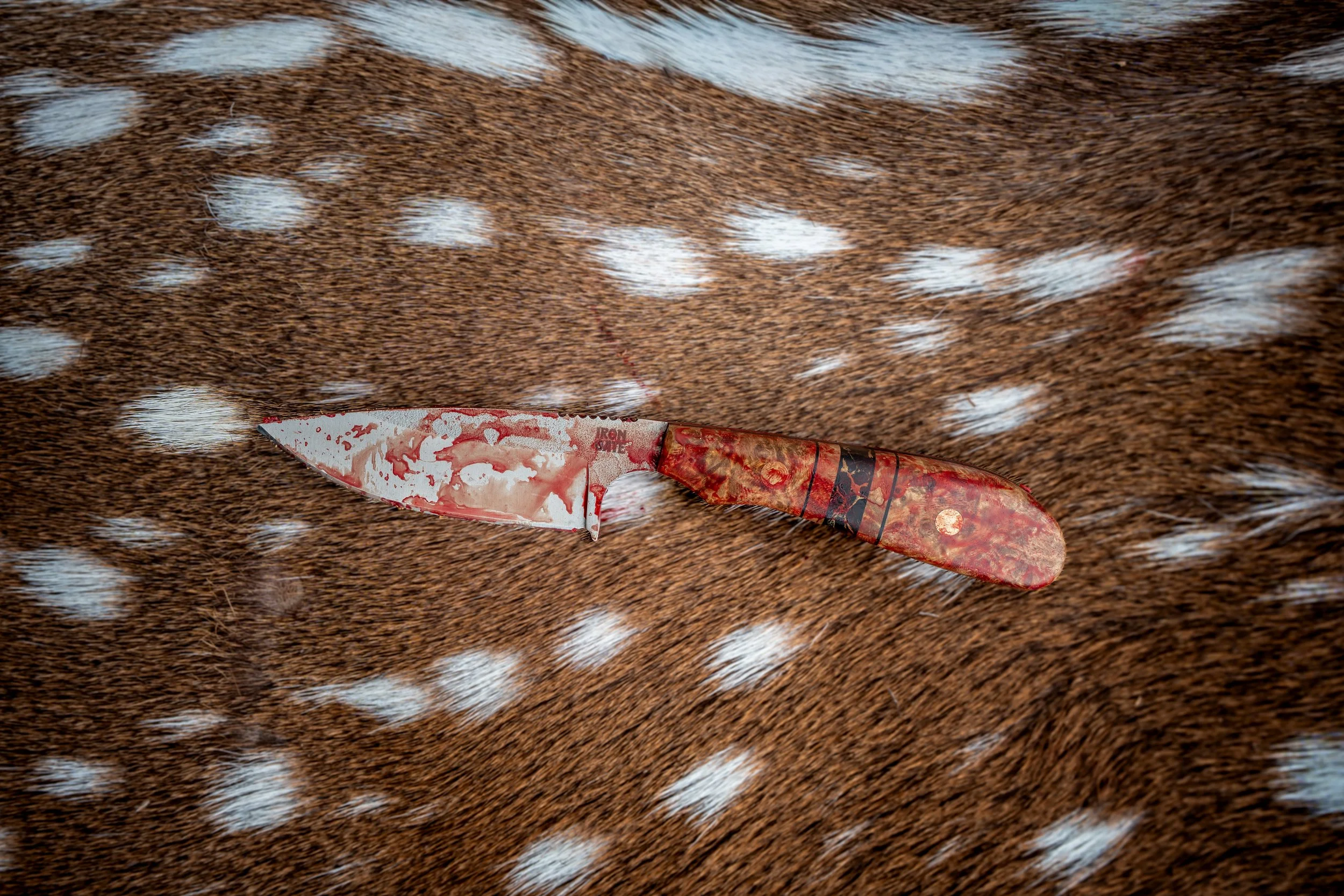 A blood-stained folding knife resting on a brown and white patterned fur surface.