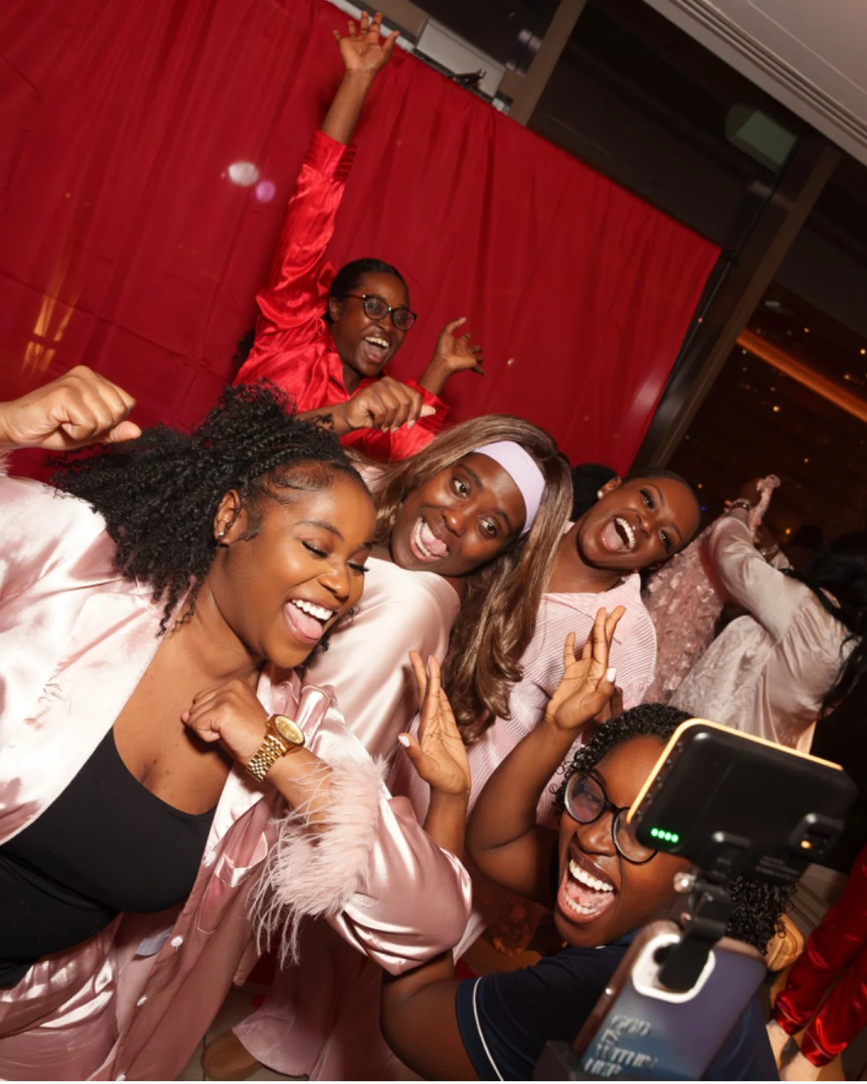 Group of women celebrating and taking a selfie at a party, smiling and making joyful gestures.
