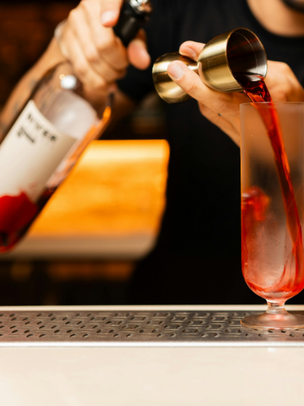 Someone pouring a red mocktail from a shaker into a tall glass.