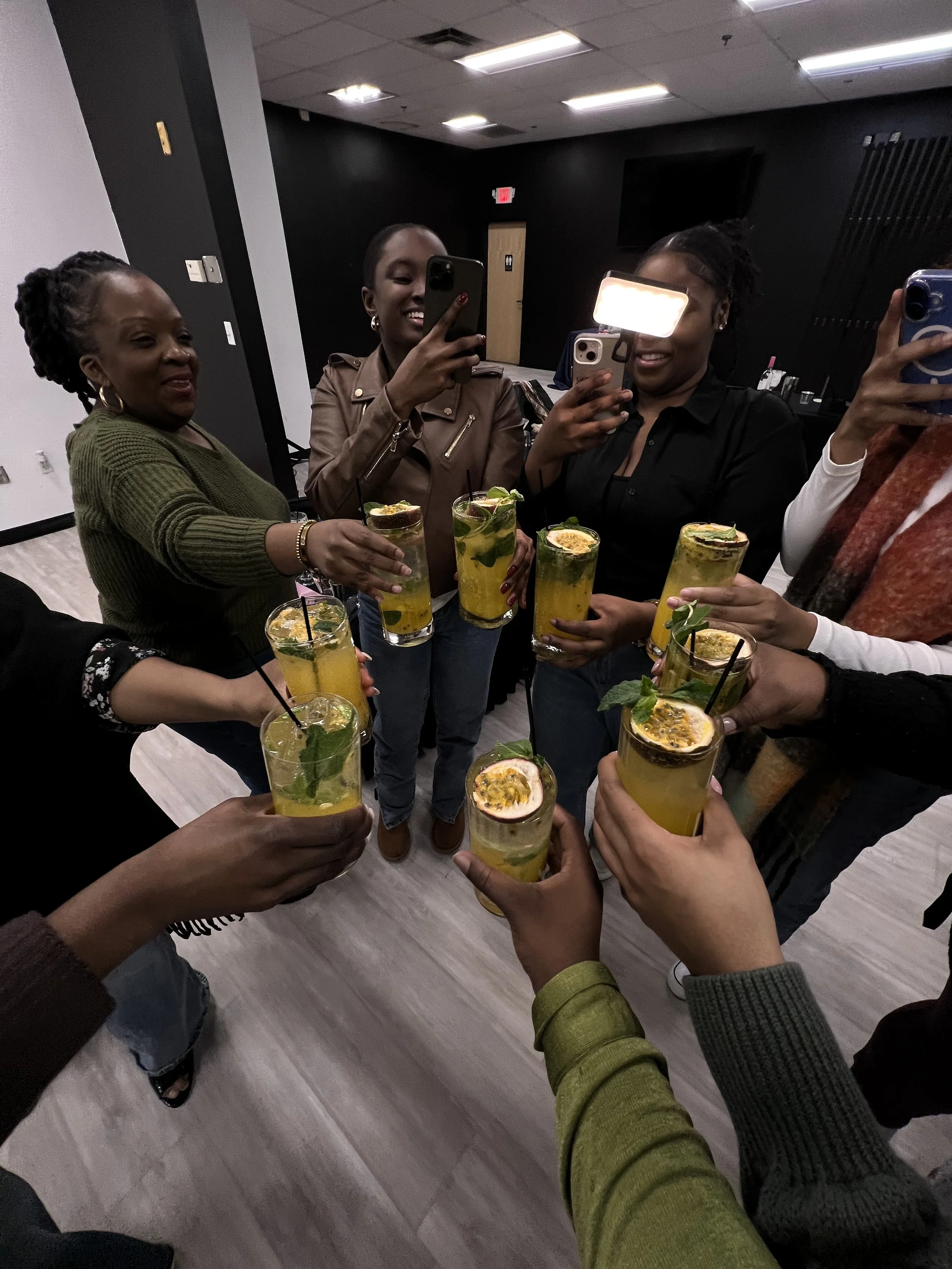 People holding yellow cocktails with passion fruit and mint in a group at an indoor gathering.