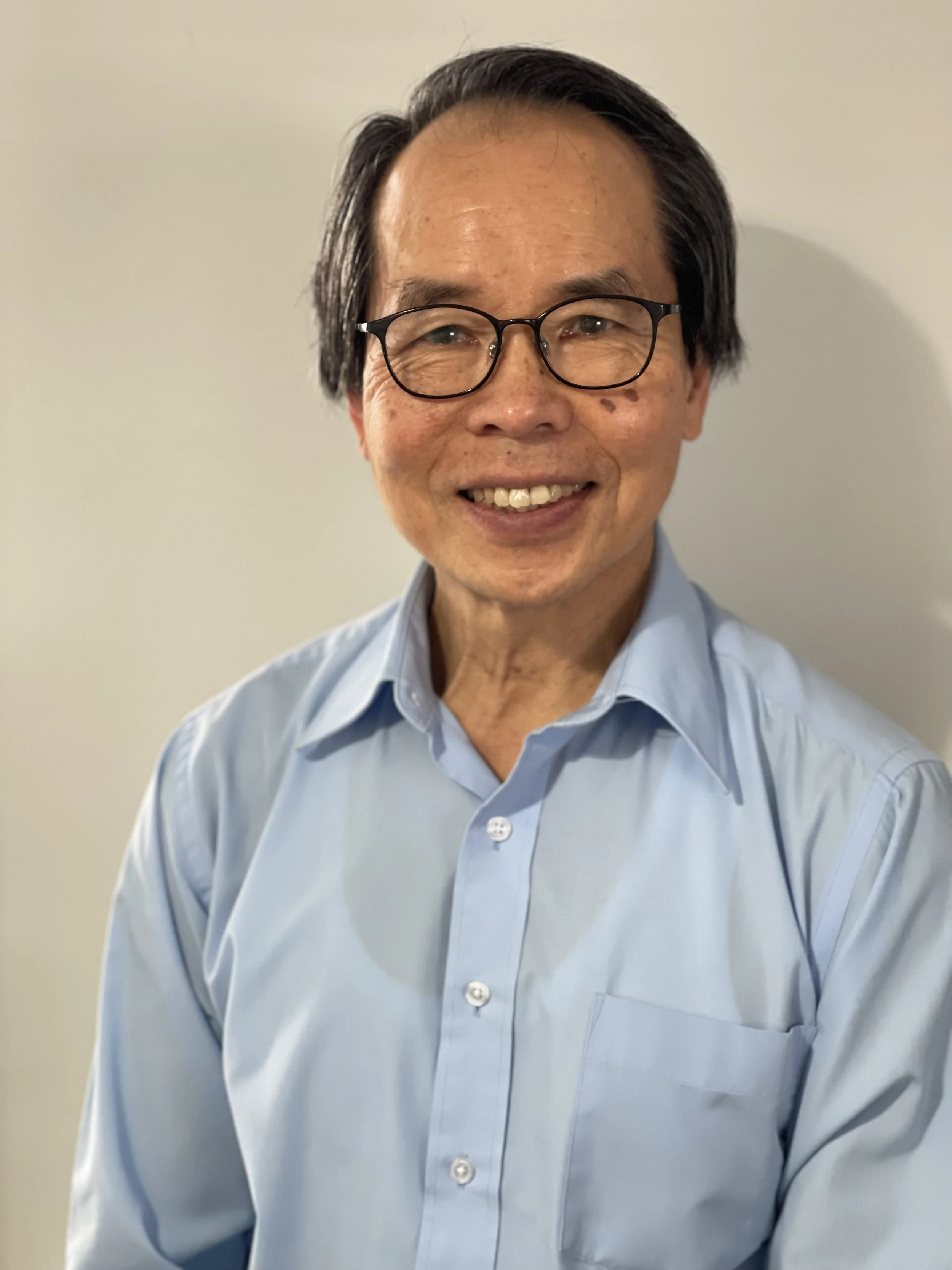 Stephen Yao in front of a white background wearing glasses and a blue button down shirt