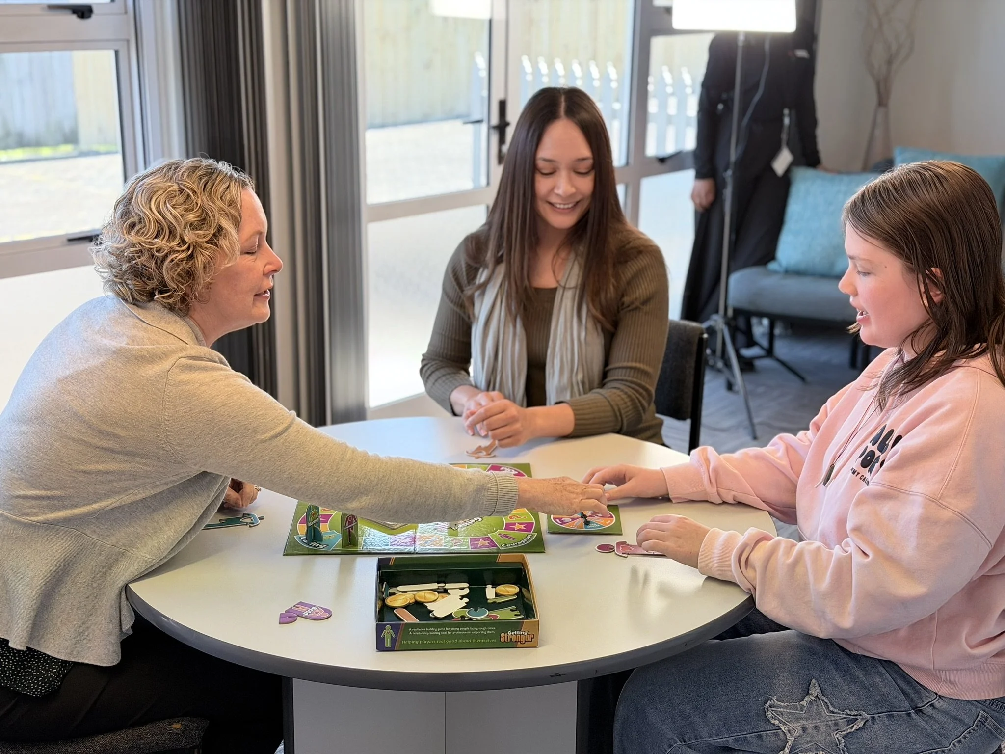 Two women and a child sitting at a white table playing a game at the pakuranga counselling centre