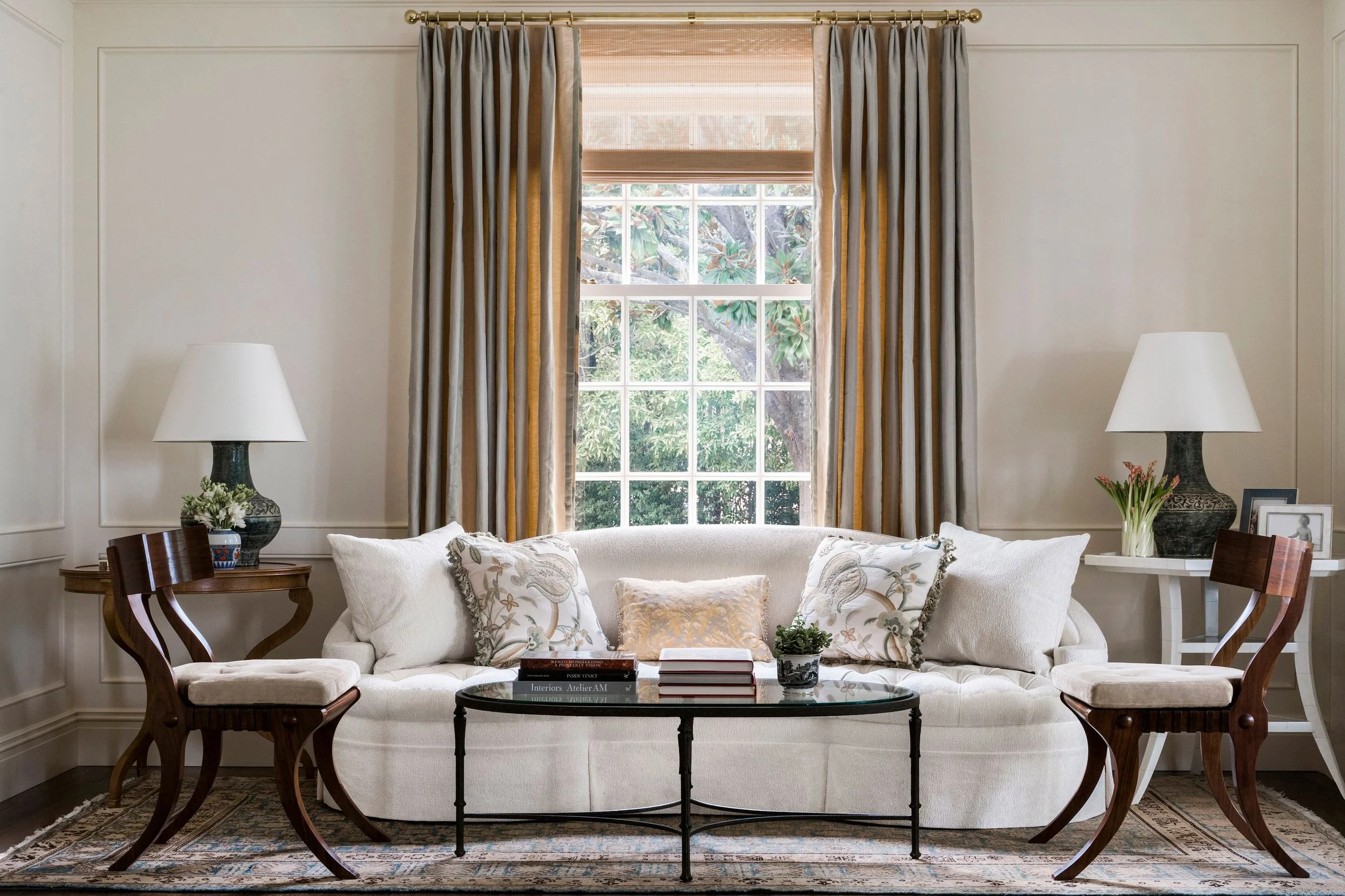 Sofa with patterned pillows beneath a window with striped drapery and woven shade