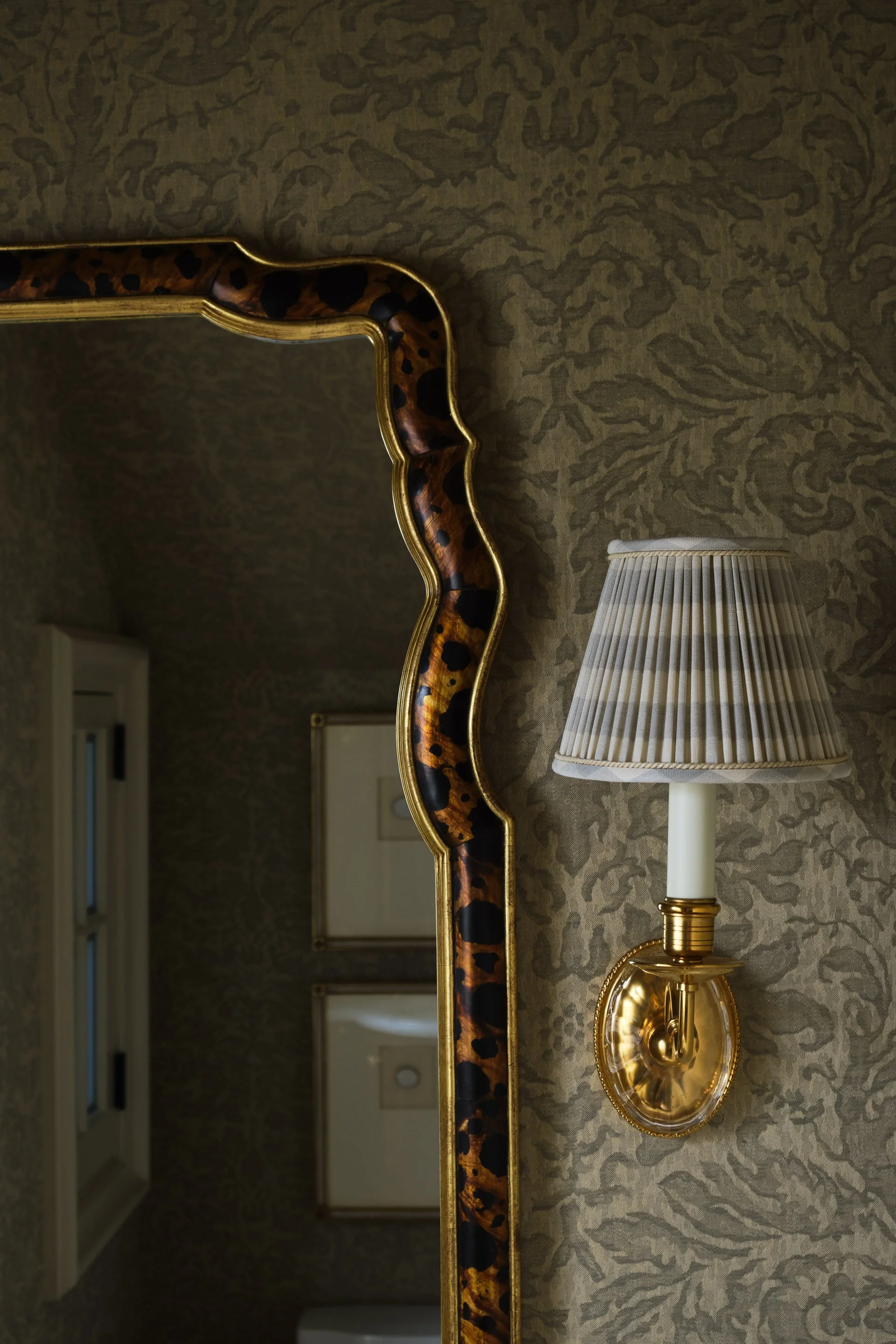 Powder room detail with scalloped gilt mirror, pleated sconce, and patterned wallpaper
