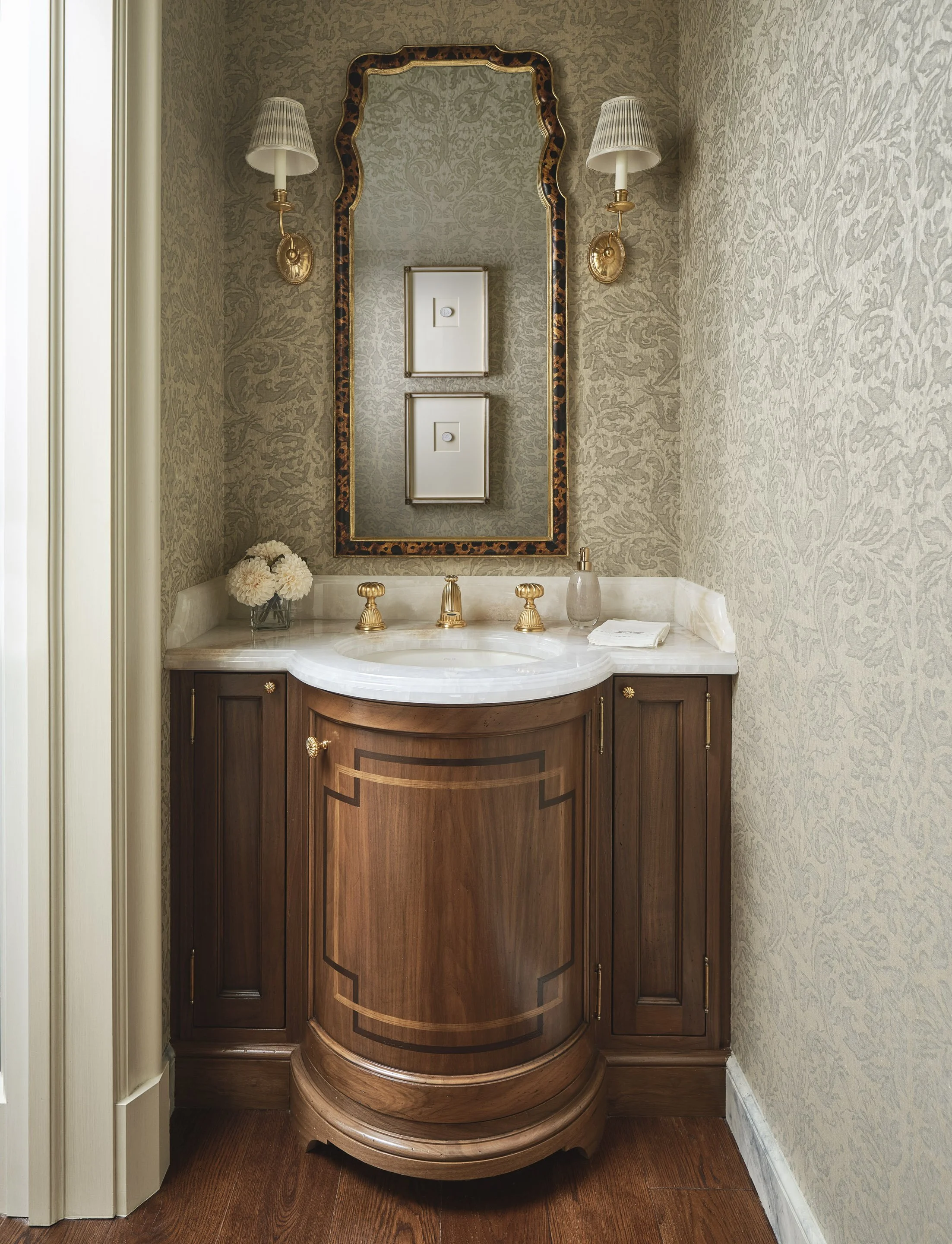 Powder room with curved wood vanity, marble top, and brass fixtures
