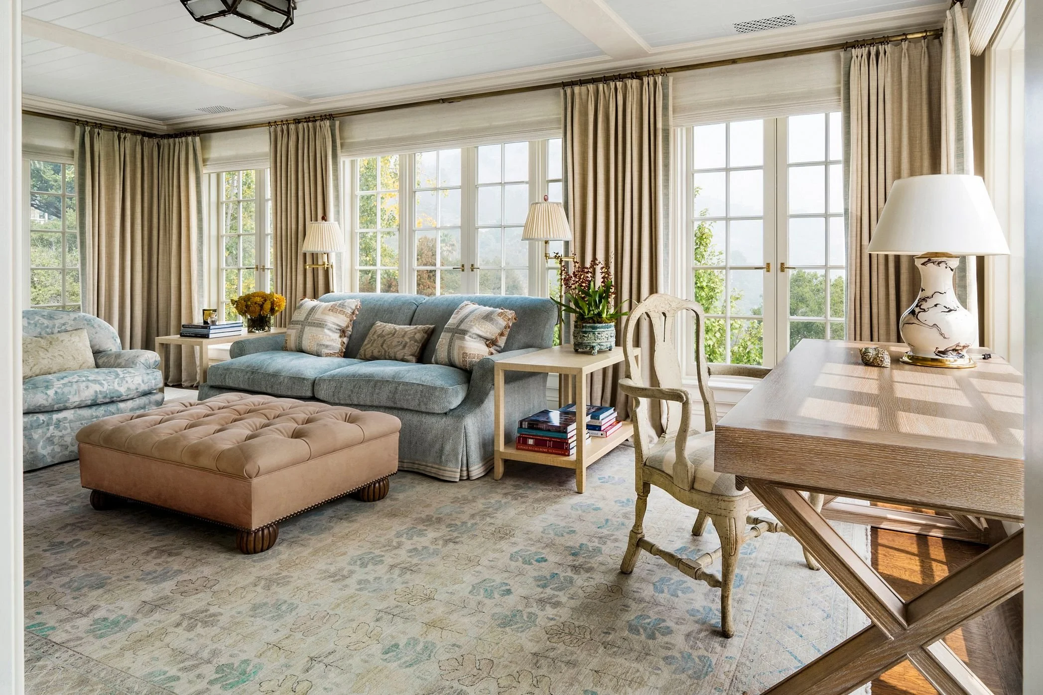 Living room with blue sofa, leather ottoman, and full-height drapery, East Coast Georgian