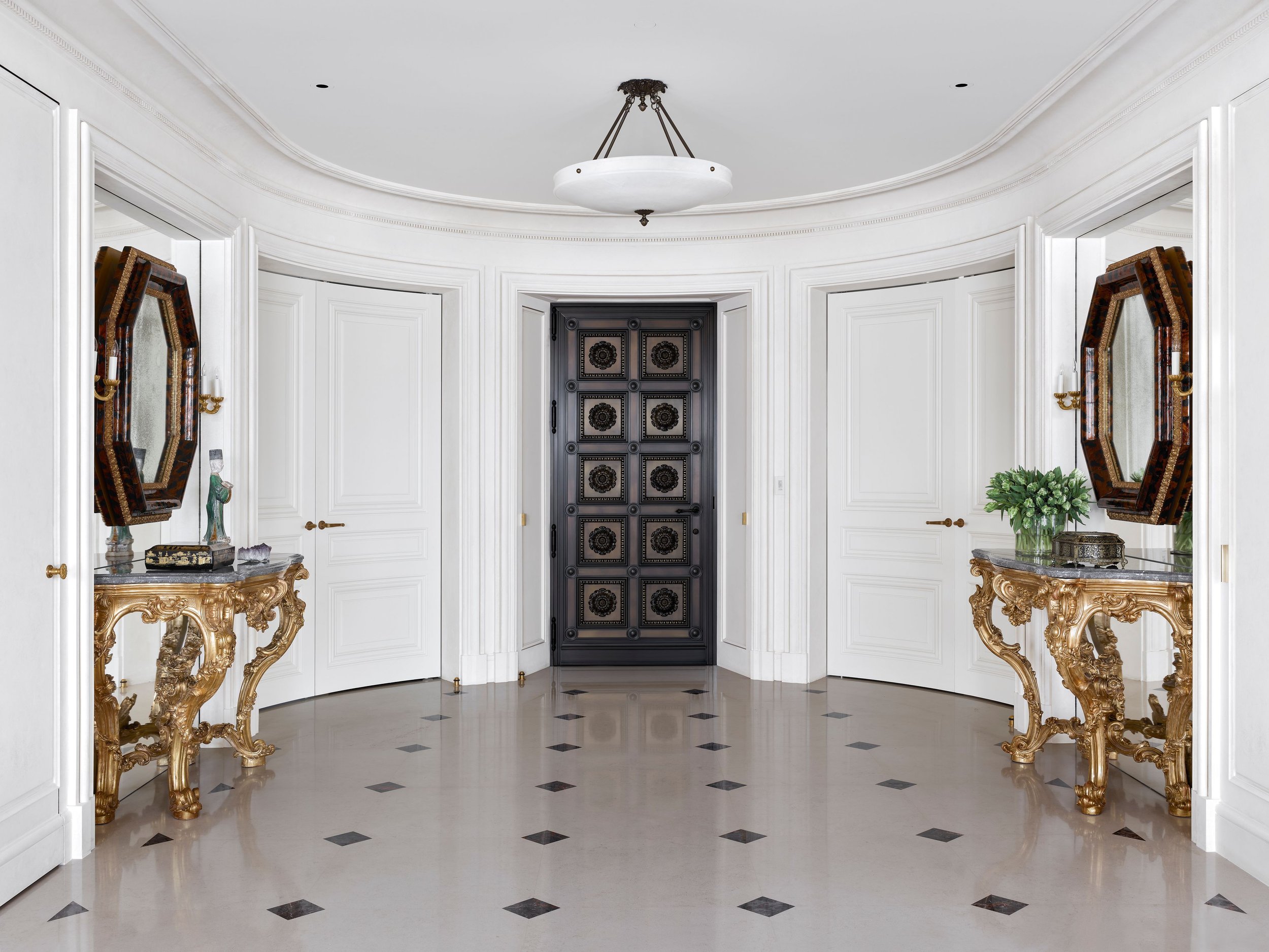 Oval entry hall with black and white marble floor, paneled doors, and gilt consoles