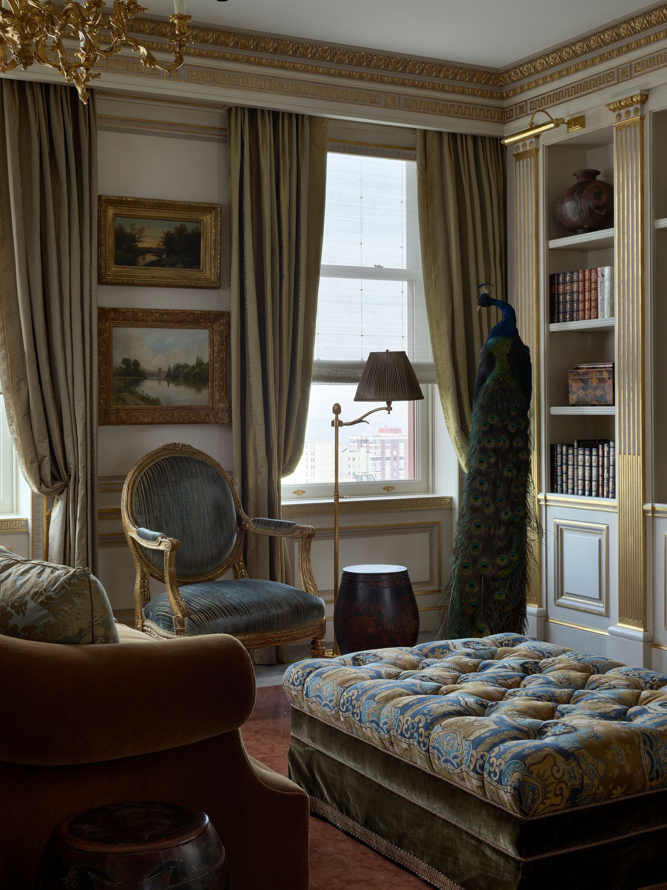 Sitting room with layered paintings, peacock sculpture, and blue upholstered ottoman, Classic French Apartment