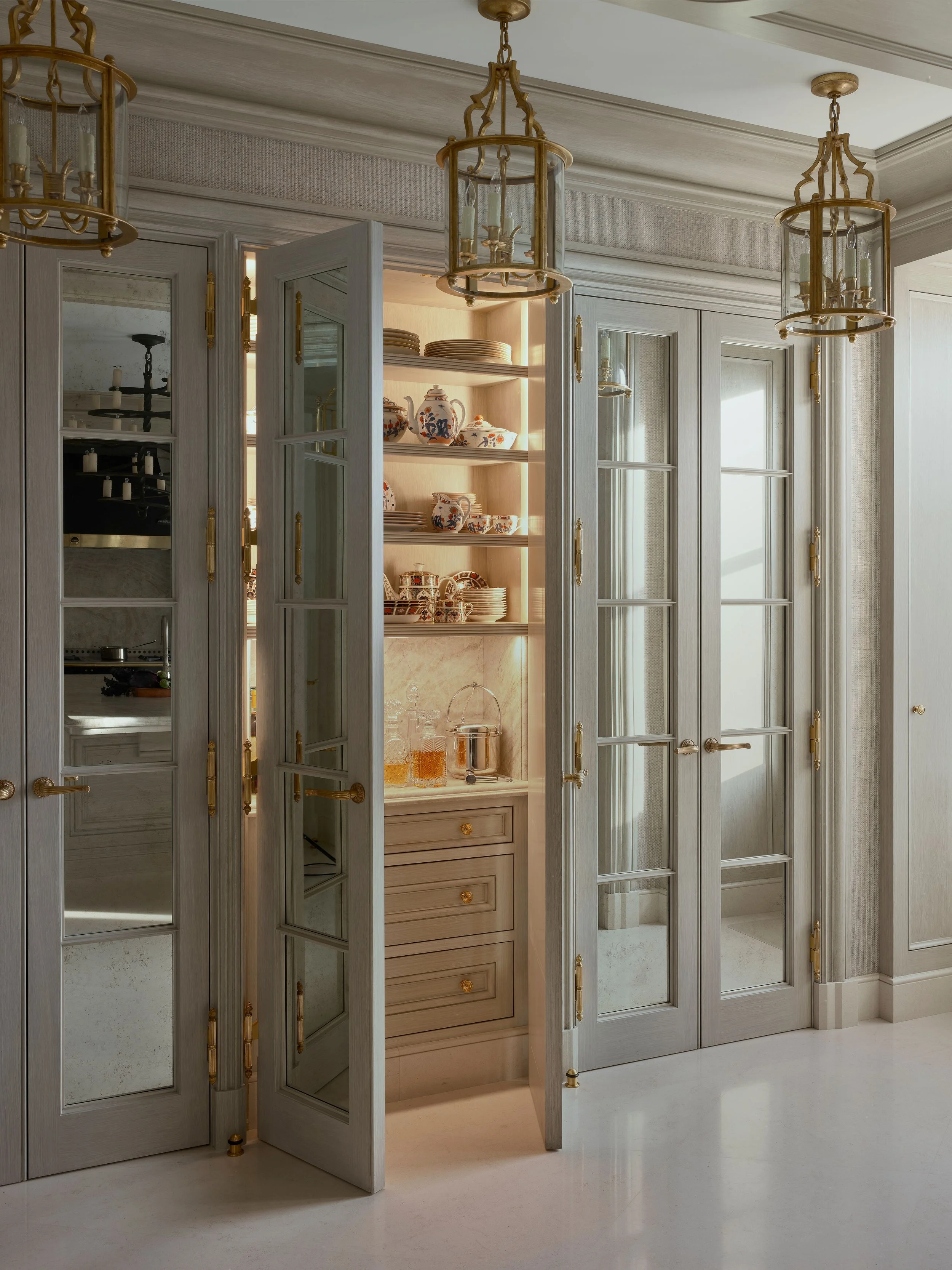 Mirrored glass-front pantry cabinets with brass hardware