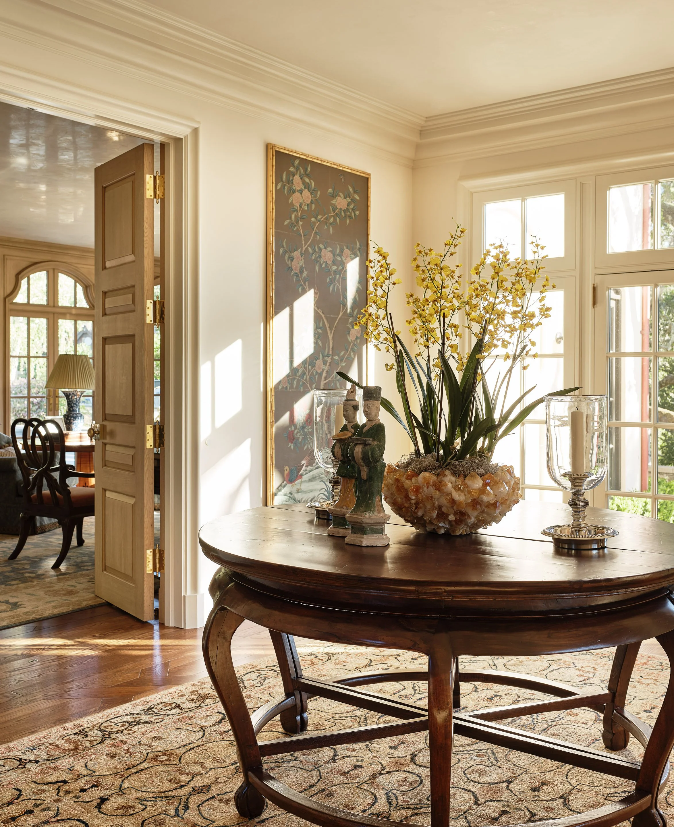 Entry hall with round antique table and yellow orchids in afternoon light