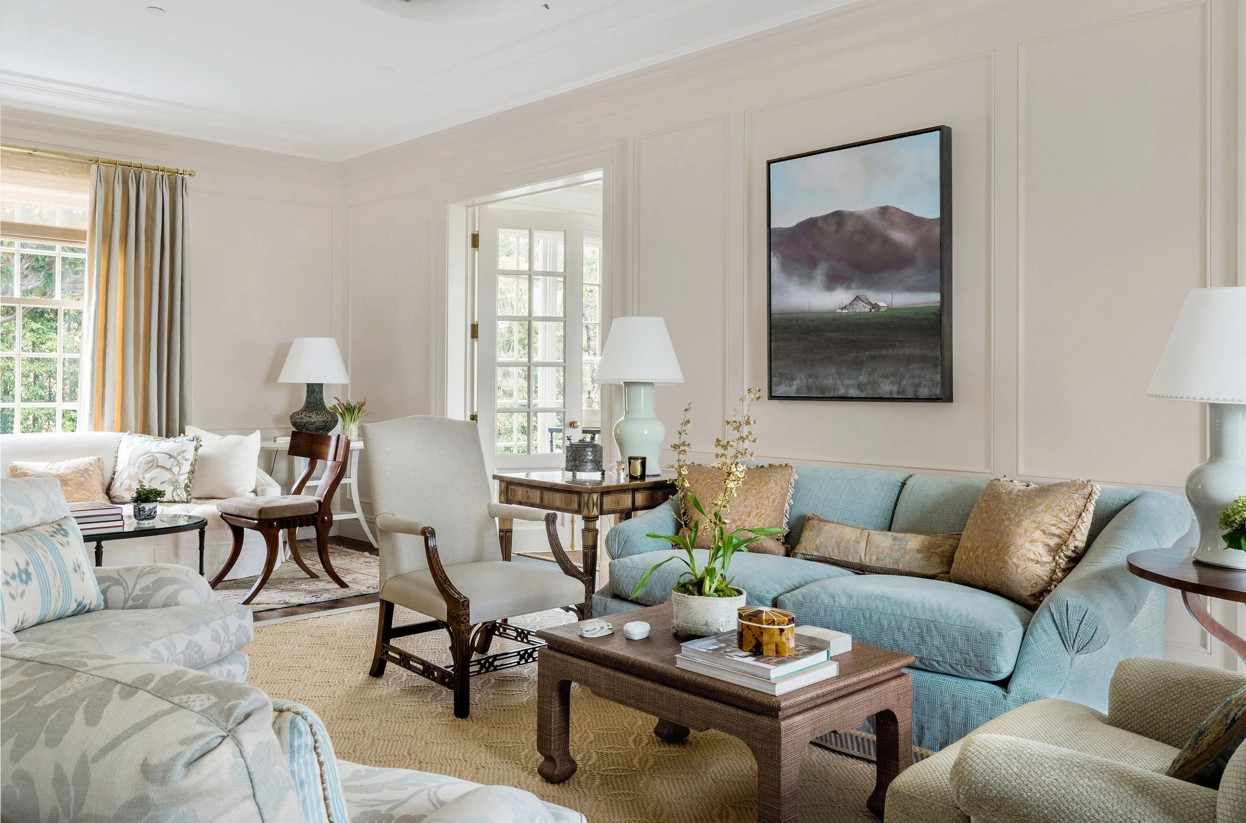 Living room with blue sectional, mahogany coffee table, and landscape painting, East Coast Georgian
