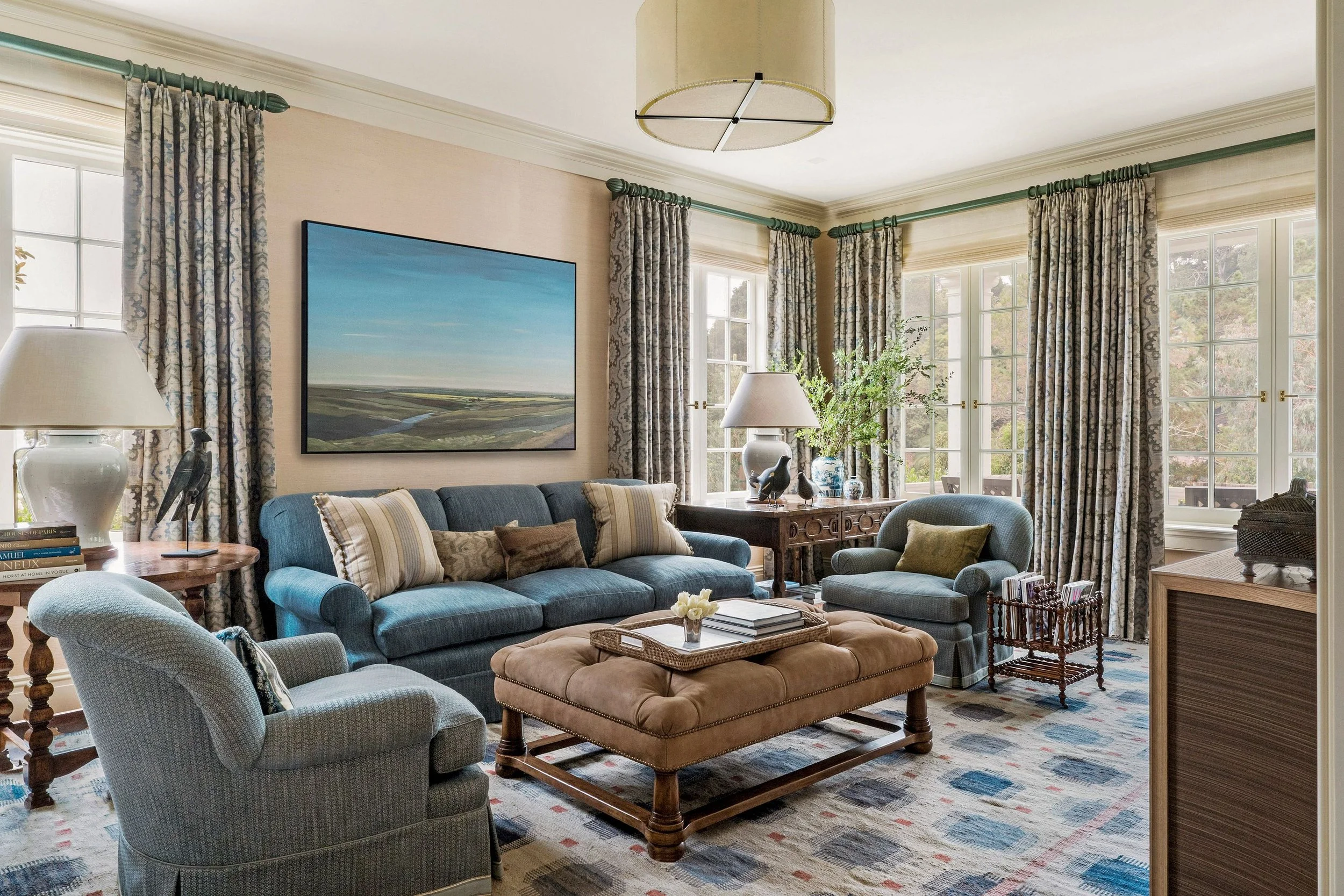 Family room with blue sofas, tufted leather ottoman, and landscape painting