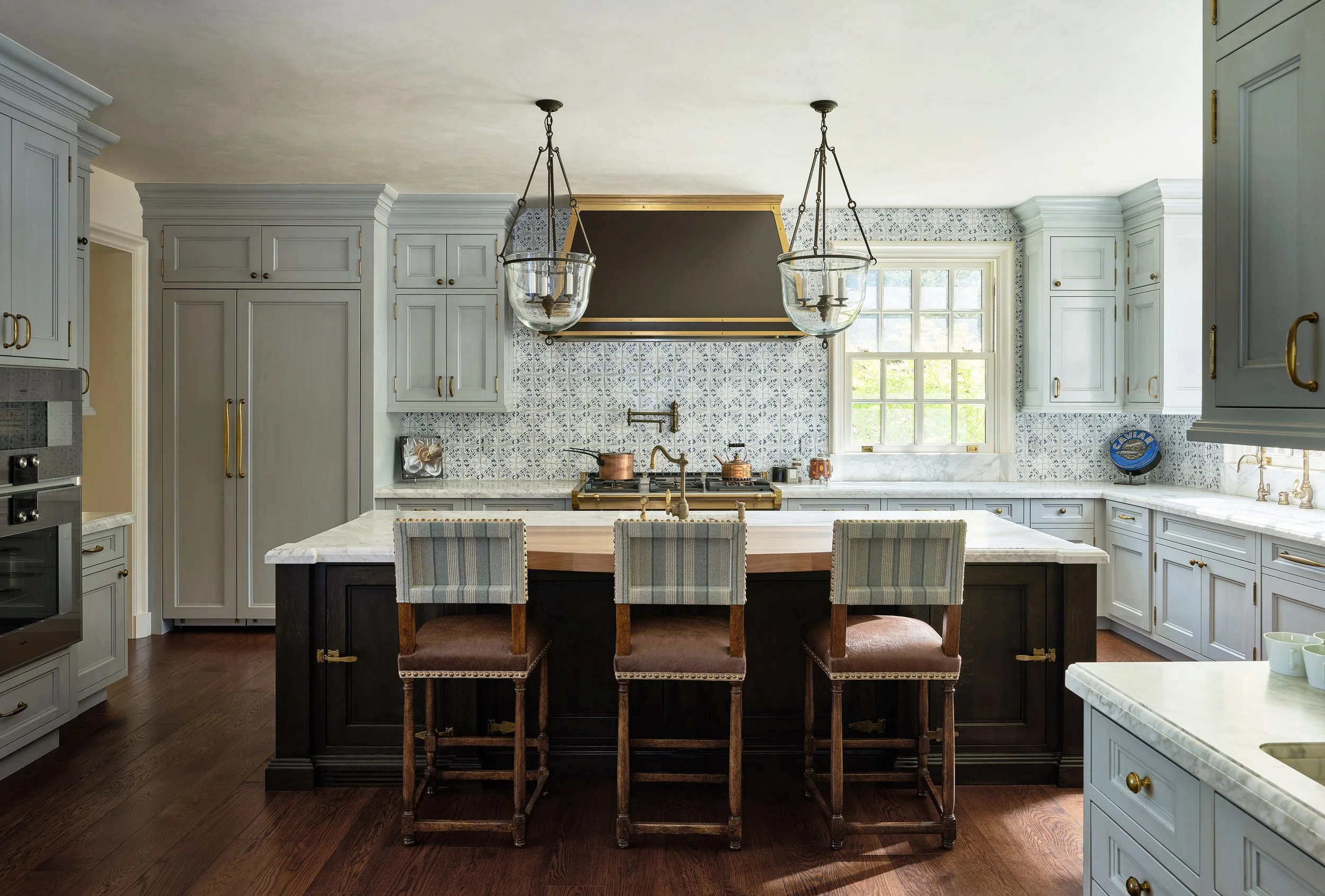 Kitchen with blue-gray cabinetry, marble island, counter stools, and lantern pendants