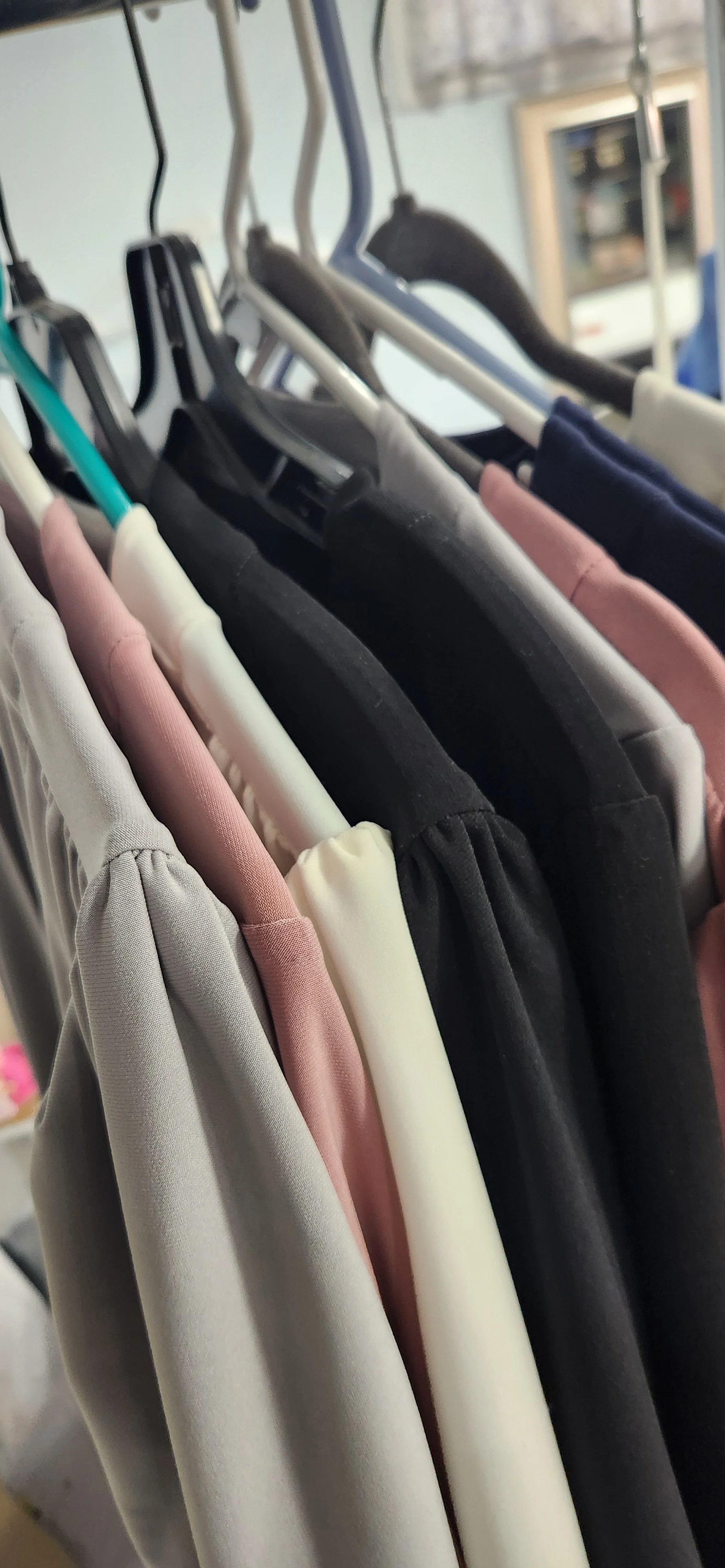 Clothes hanging on a rack, including pink, white, black, and navy garments, on black and white hangers.