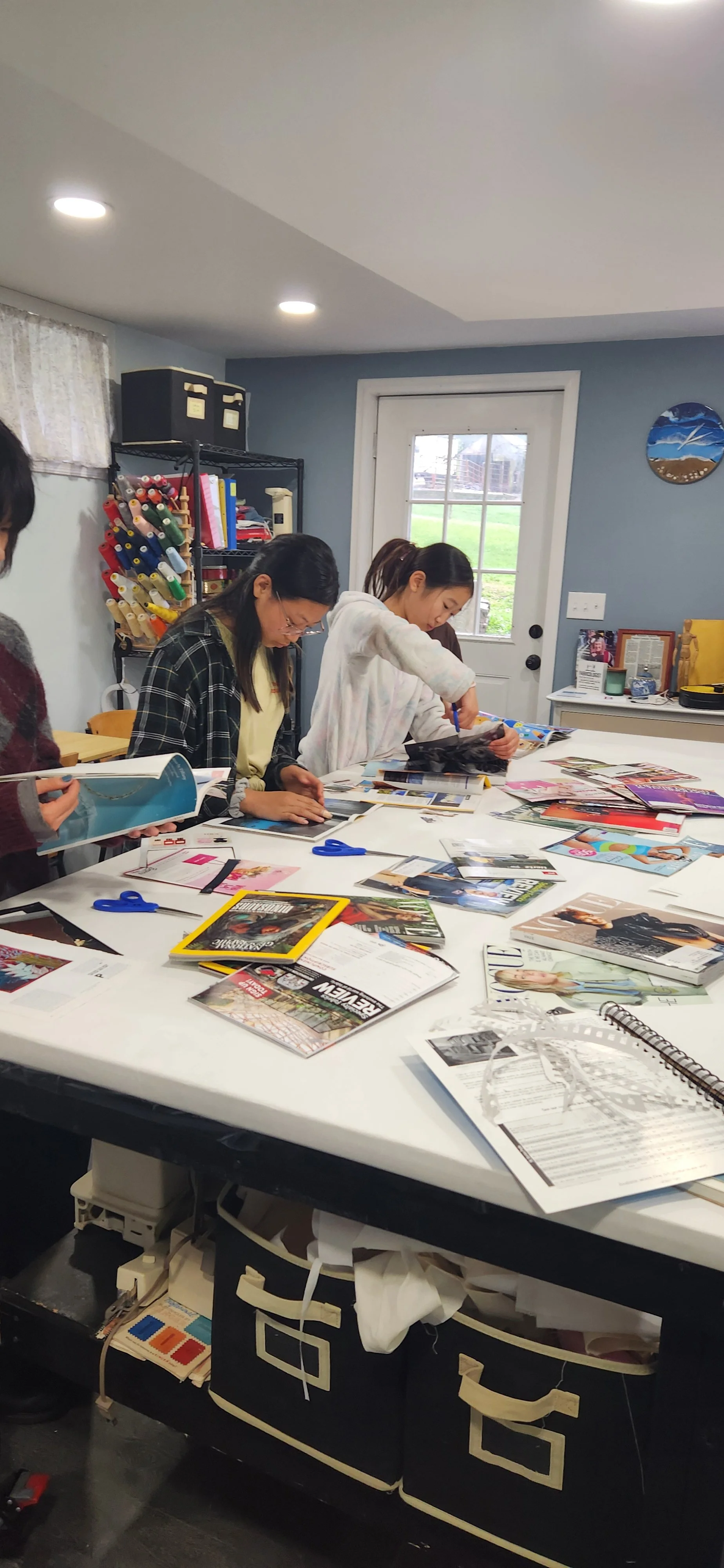 People working with magazines and materials on a large white table in a well-lit room.