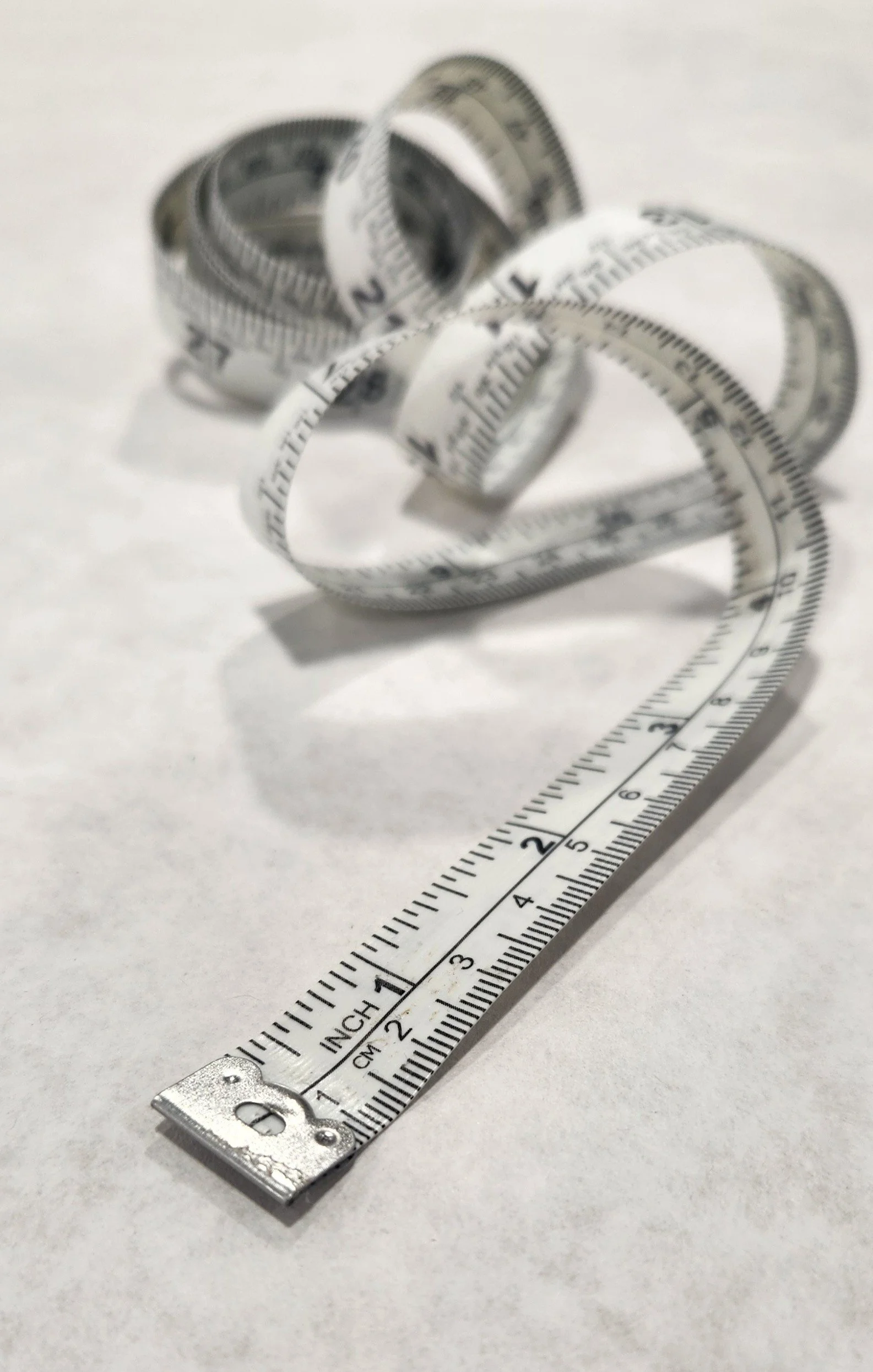 A metallic folding ruler extended on a white surface, with multiple curved measuring tapes placed on top of it.