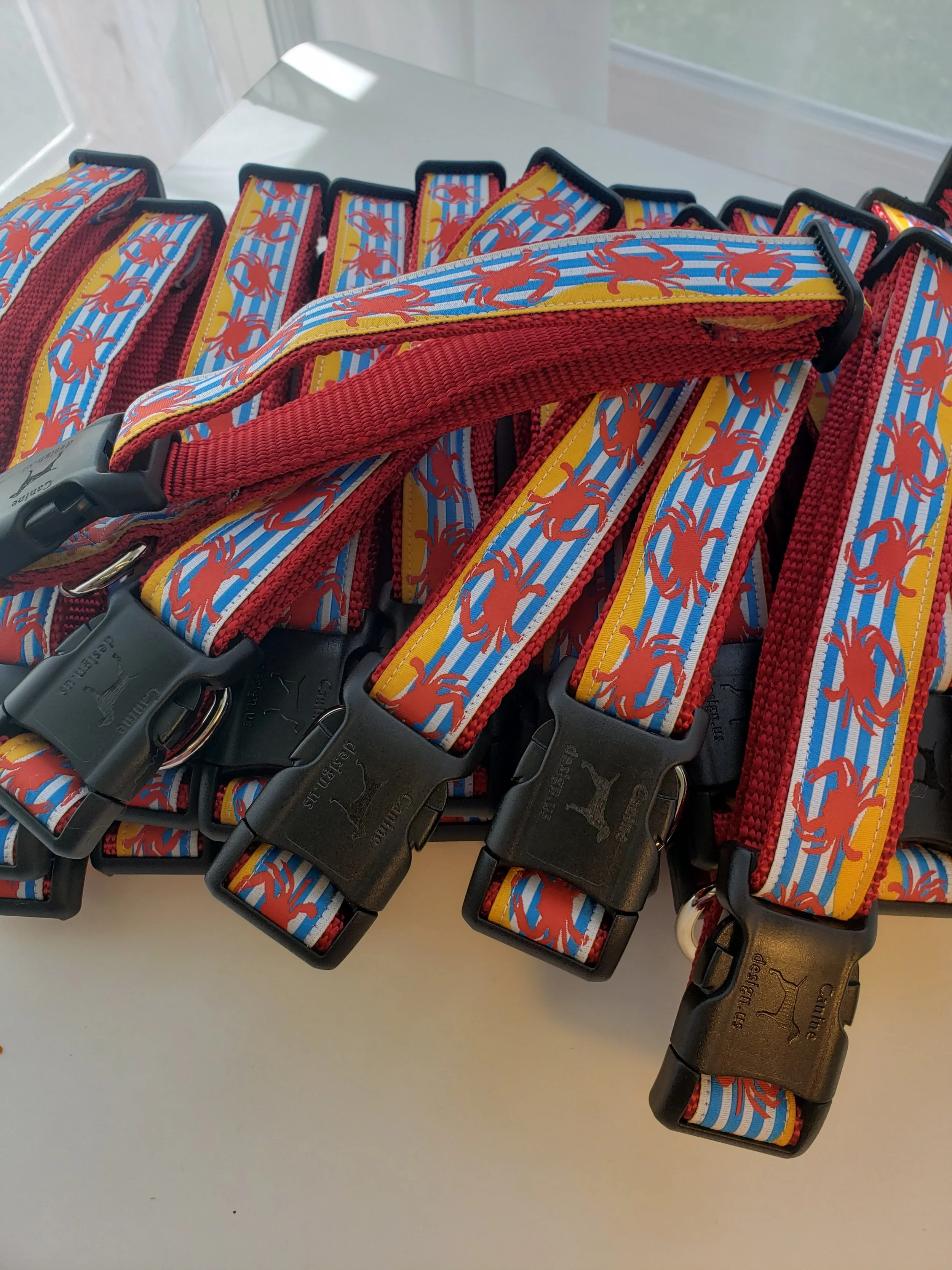 Multiple colorful dog collars with a red crab pattern and black plastic buckle, arranged on a white surface.