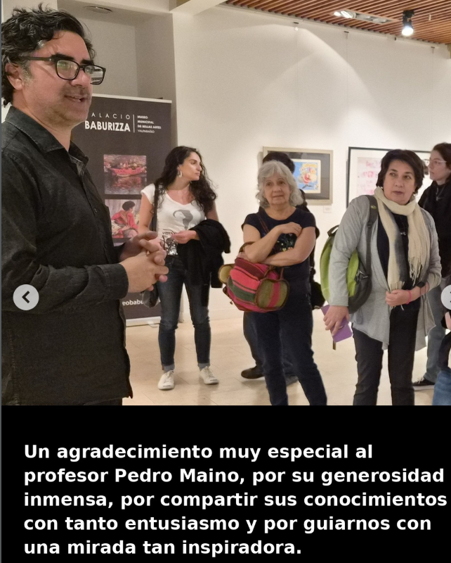 Grupo de personas en una galería de arte, una de ellas hablando y las demás escuchando, con obras de arte en las paredes y un cartel que dice 'Palacio Baburizza'.