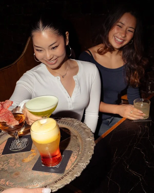 Two women smiling and enjoying cocktails at a bar or restaurant.