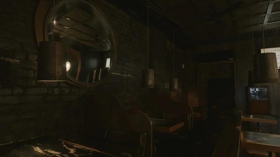 A dark, dimly lit interior space with black walls, a round mirror on the wall, hanging pendant lights, and a few chairs and tables.