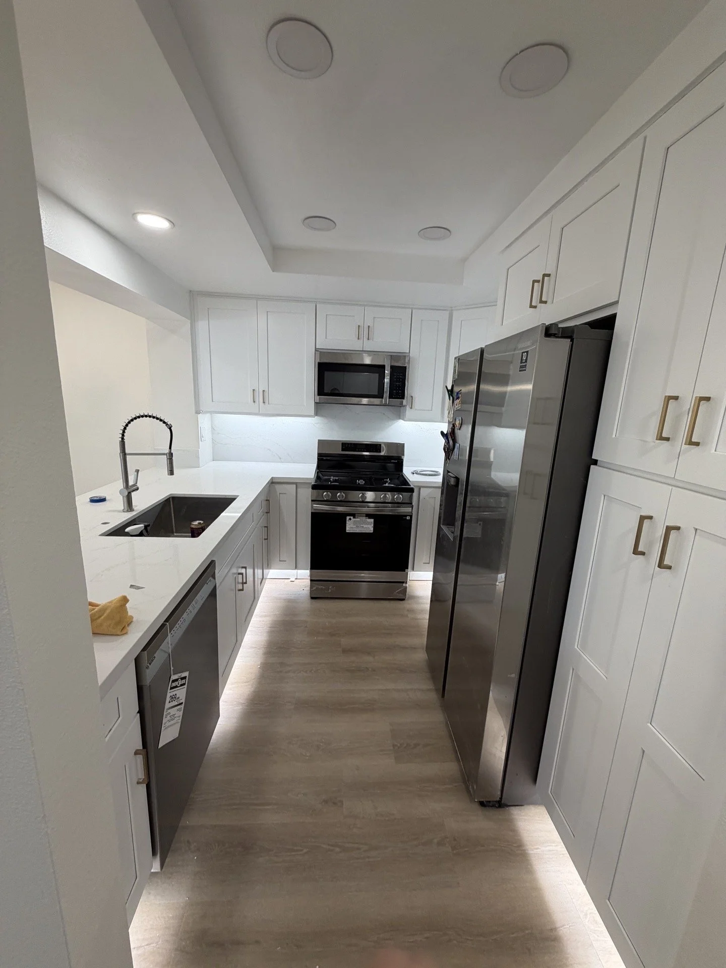 Modern kitchen with white cabinets, stainless steel refrigerator, stove, microwave, and a sink, with wood flooring and ceiling lights.