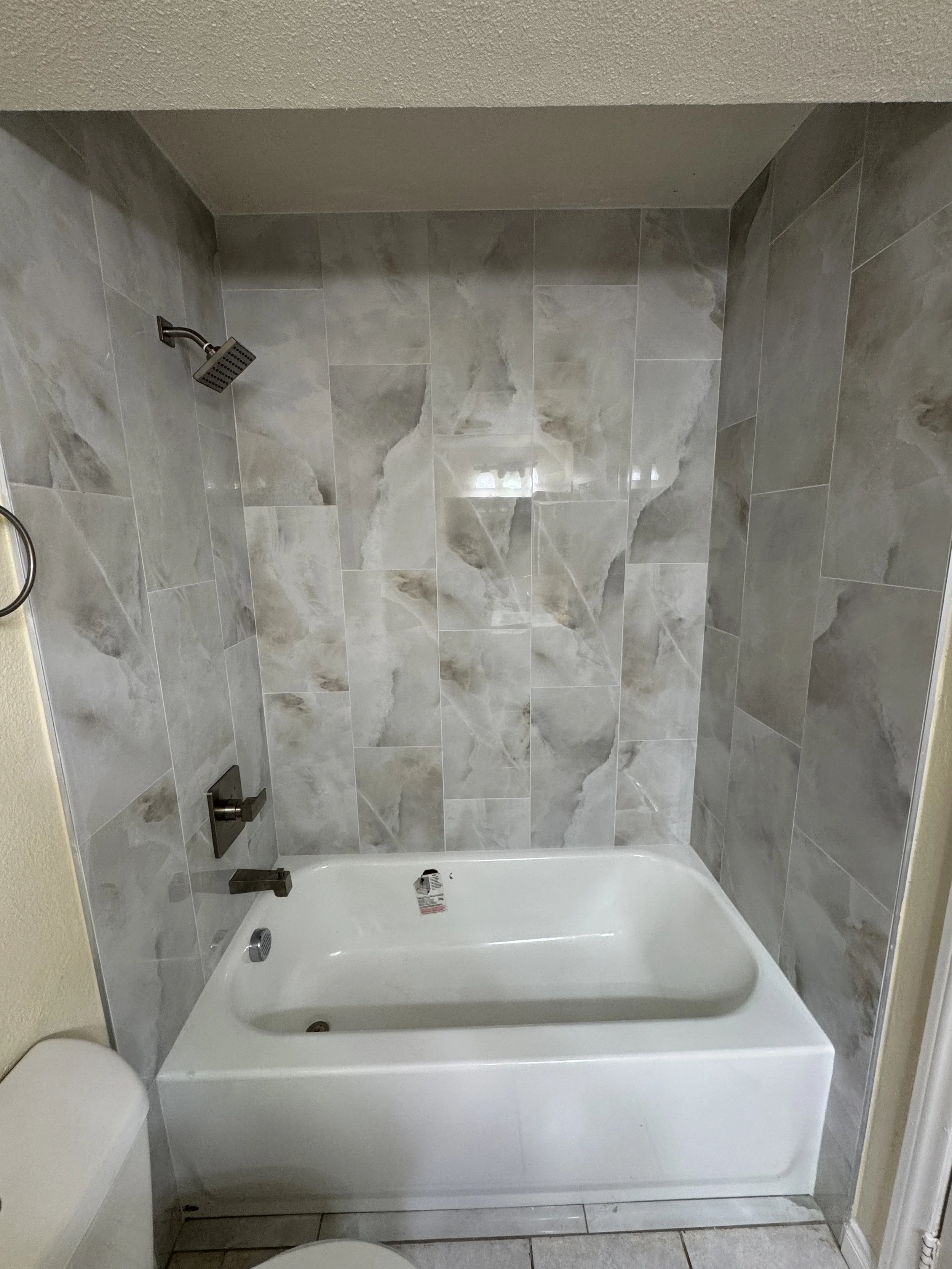 Bathroom shower with gray marble tiles, a square shower head, and a bathtub with a control panel.