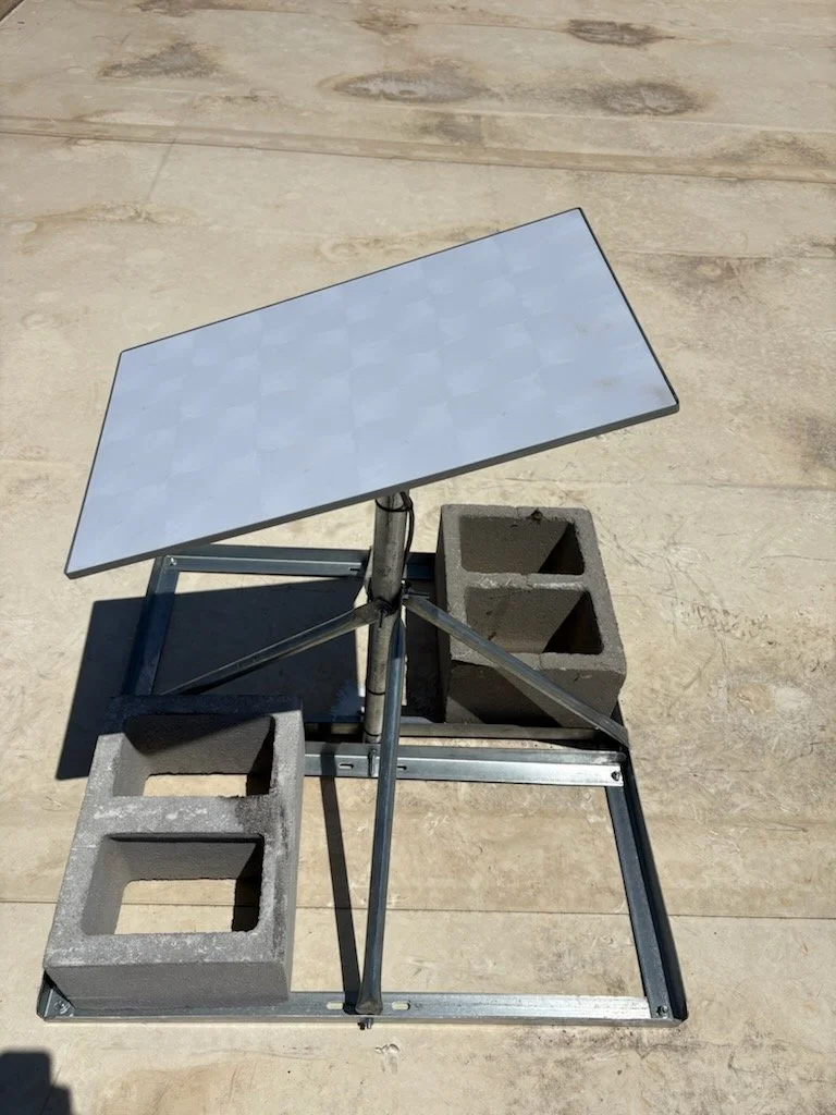 A small table with a reflective surface, two cinder blocks, and a metal frame on a concrete or pavement surface.