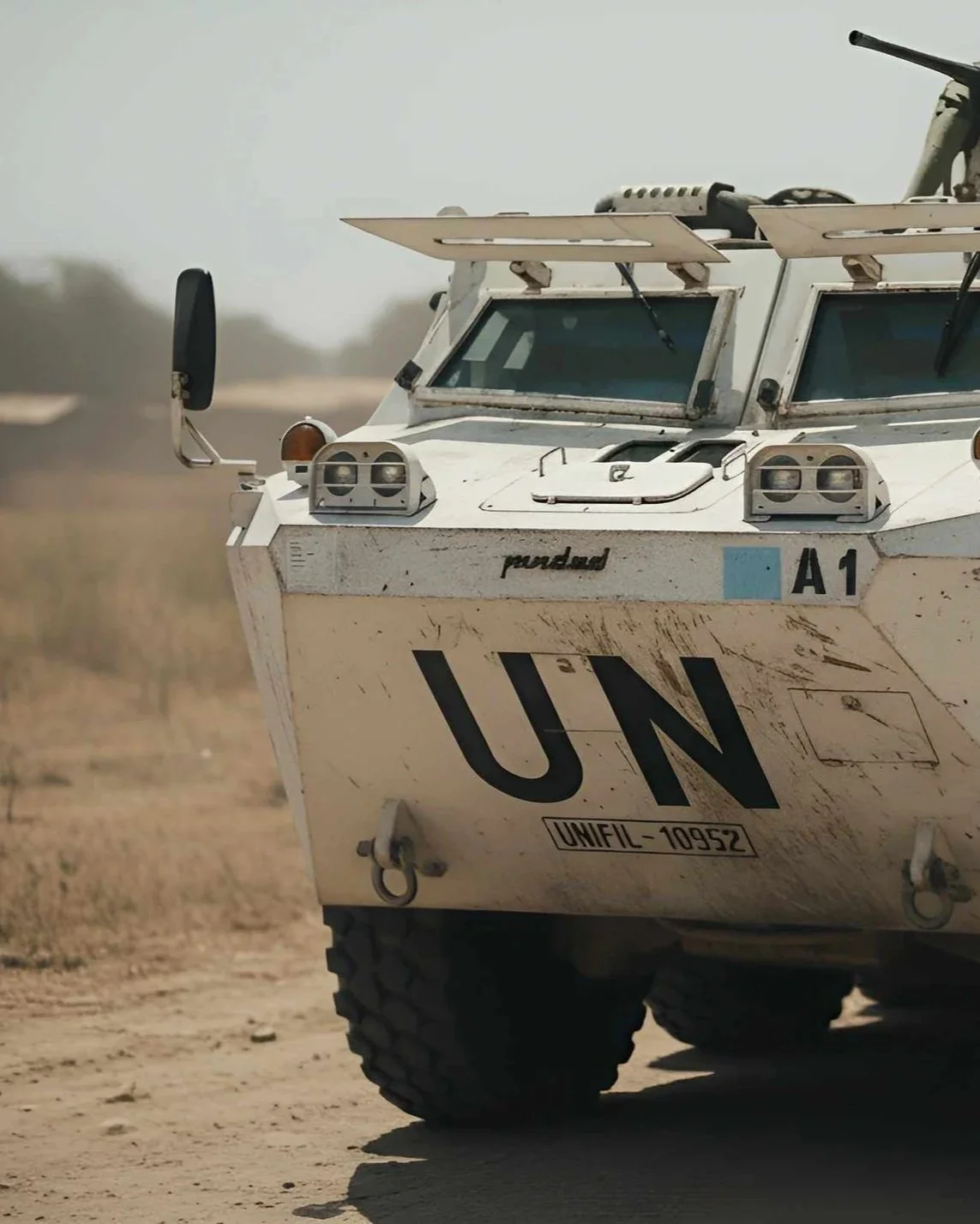 Close-up of a UN armored vehicle in desert terrain, showing front with blue and black markings, and various sensors and antennas on top.