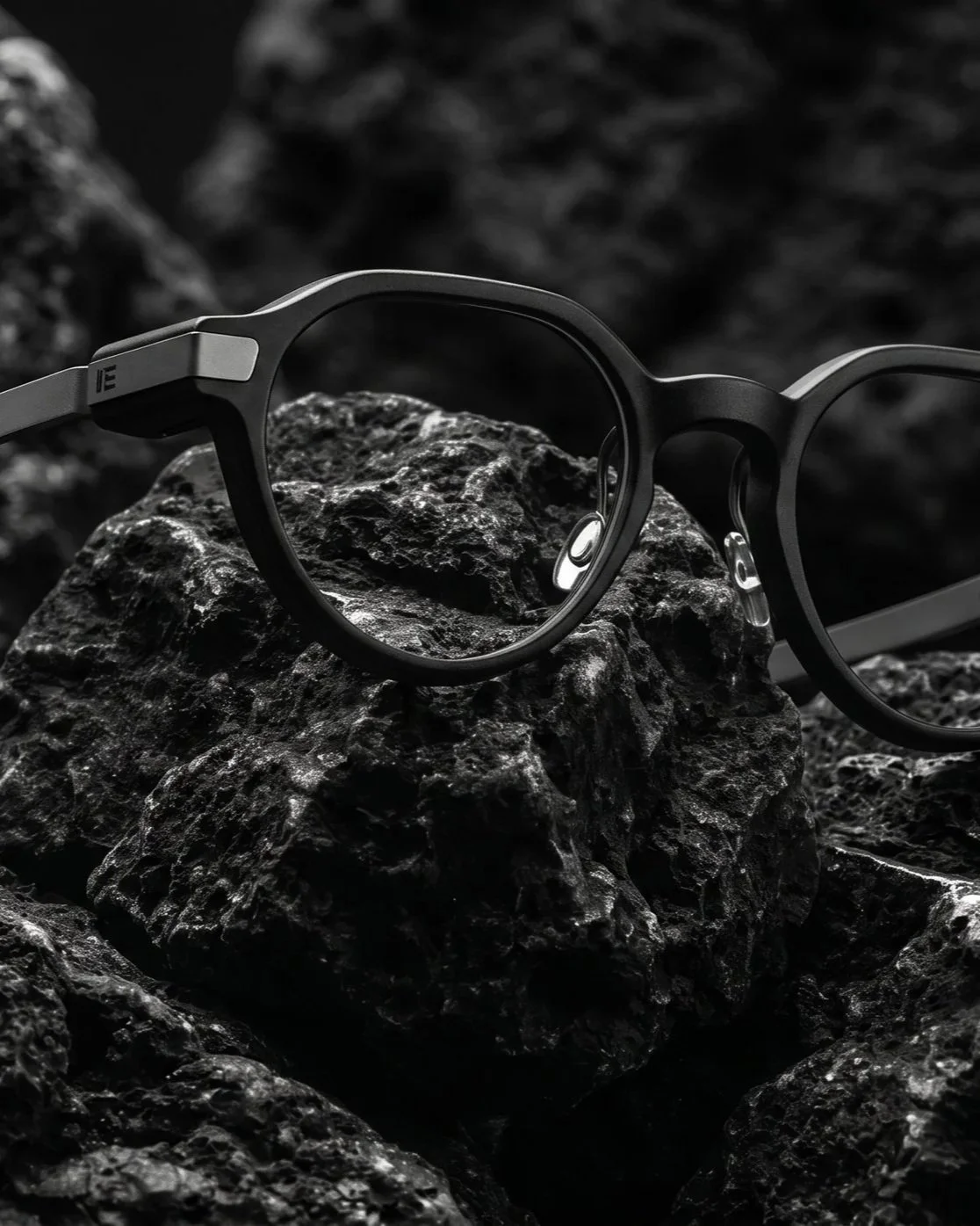 Black eyeglasses resting on rough black volcanic rocks, close-up shot in black and white.