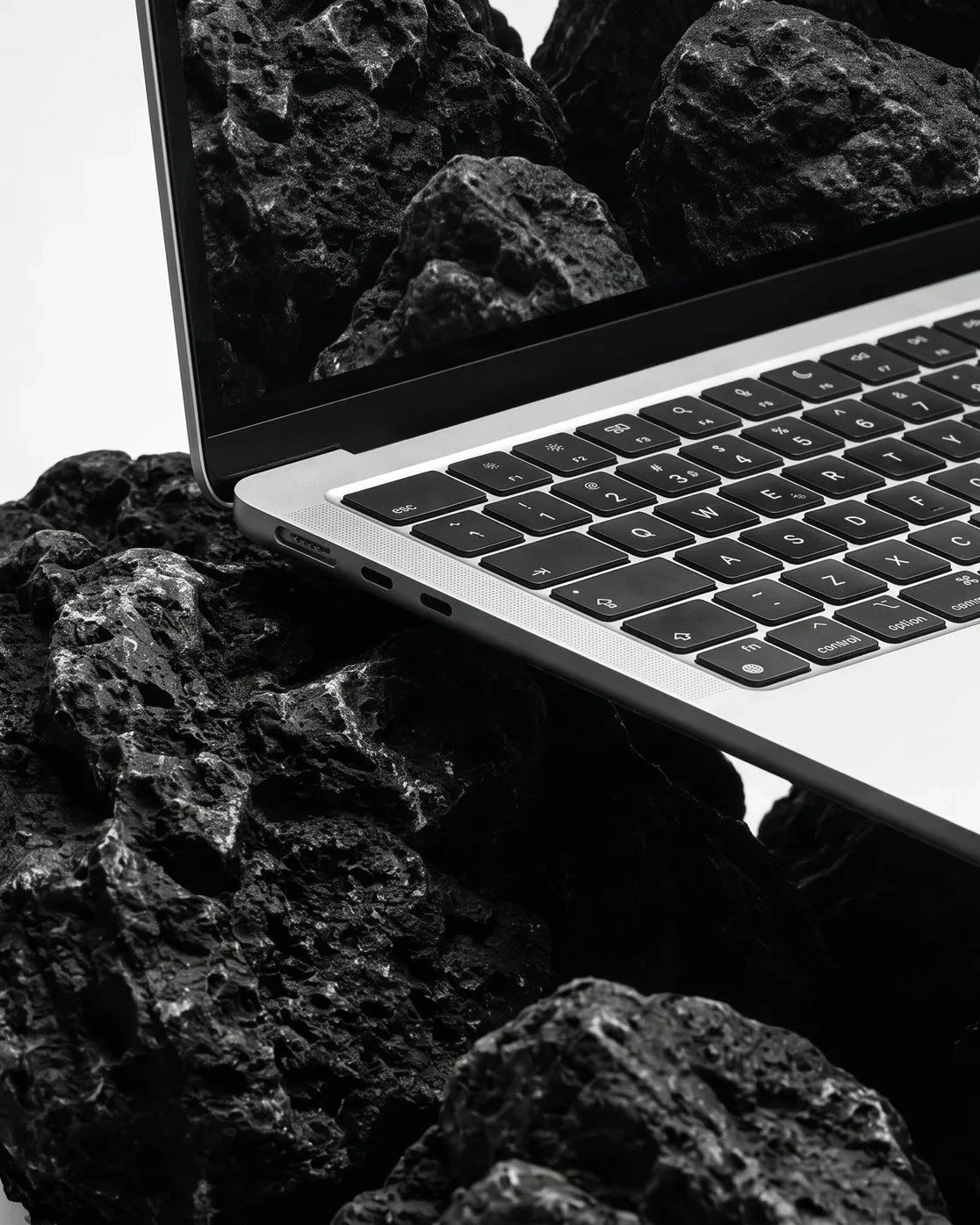 Close-up of a silver laptop with black keys on a surface of rough black volcanic rocks